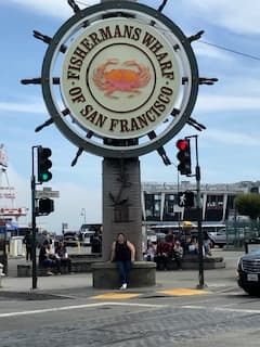 Debbie posing outdoors in front of a big sign during the daytime.