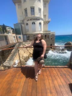 Debbie posing on a ledge outdoors by the ocean.