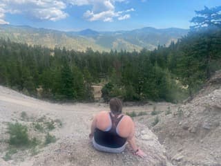 Debbie posing on top of a mountain overlooking the forest during the daytime.