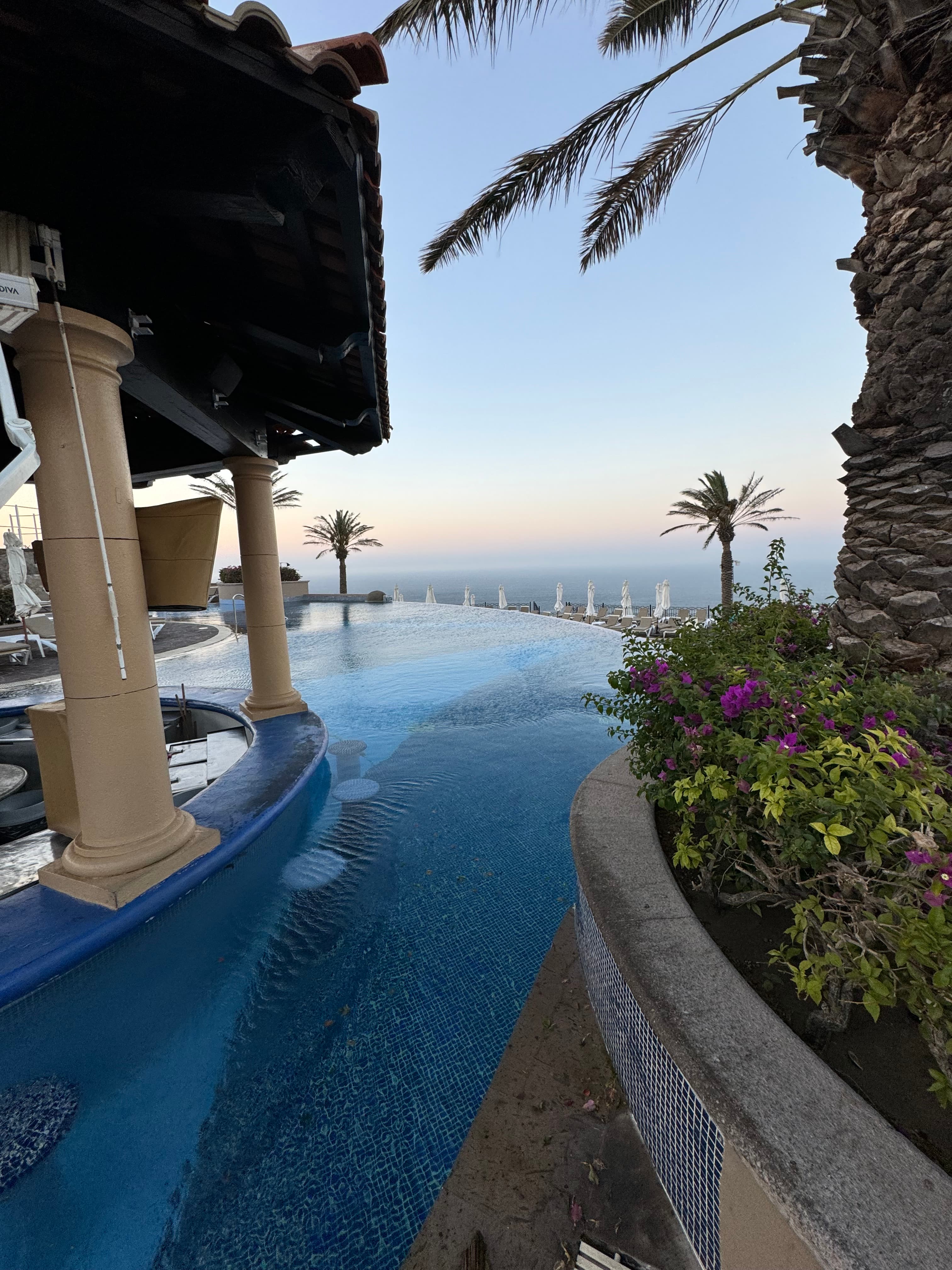 View of a resort pool and swim up bar overlooking the sea at sunset