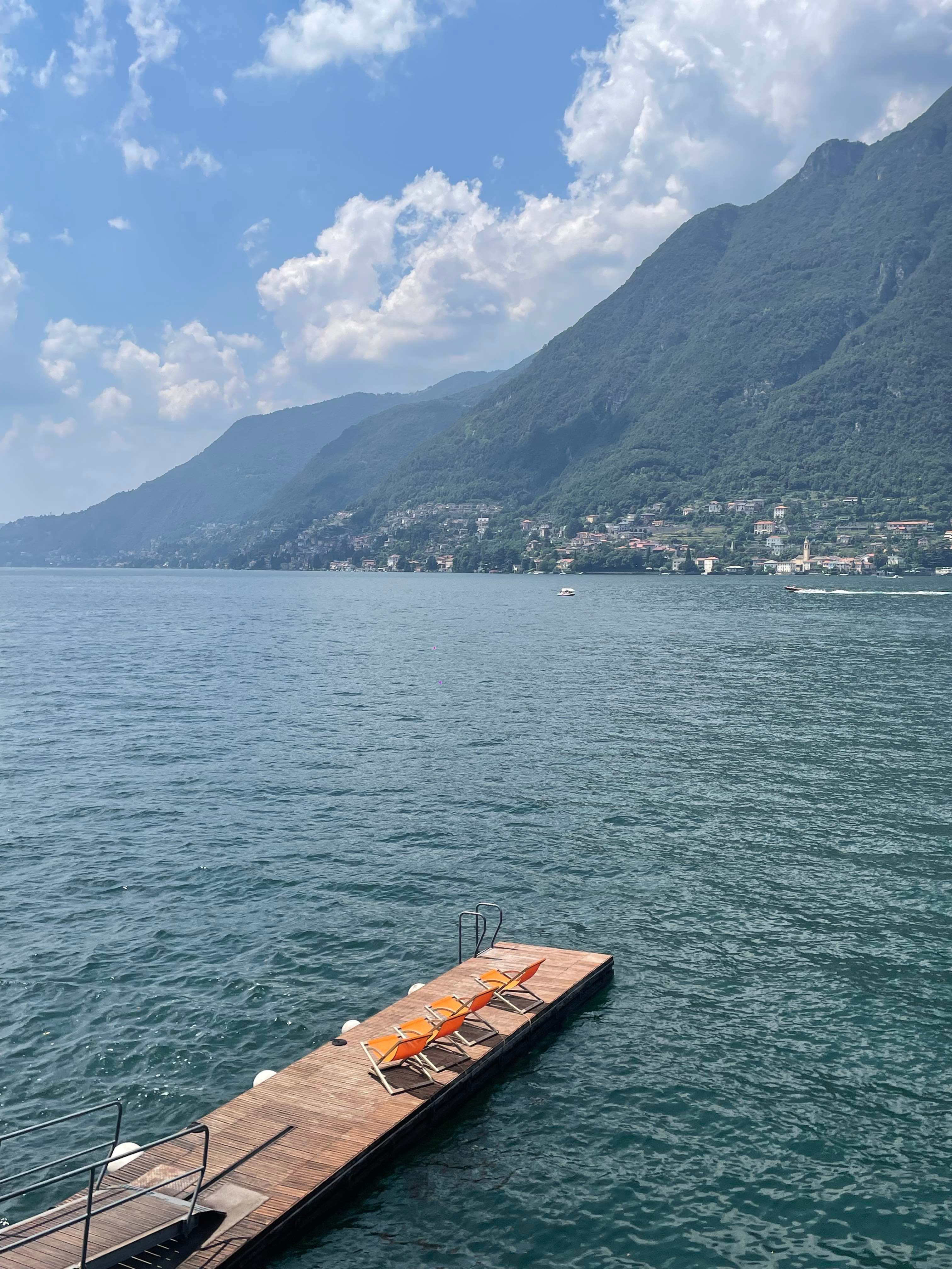 View of a wooden dock with lounge chairs and mountains on the other side of the water