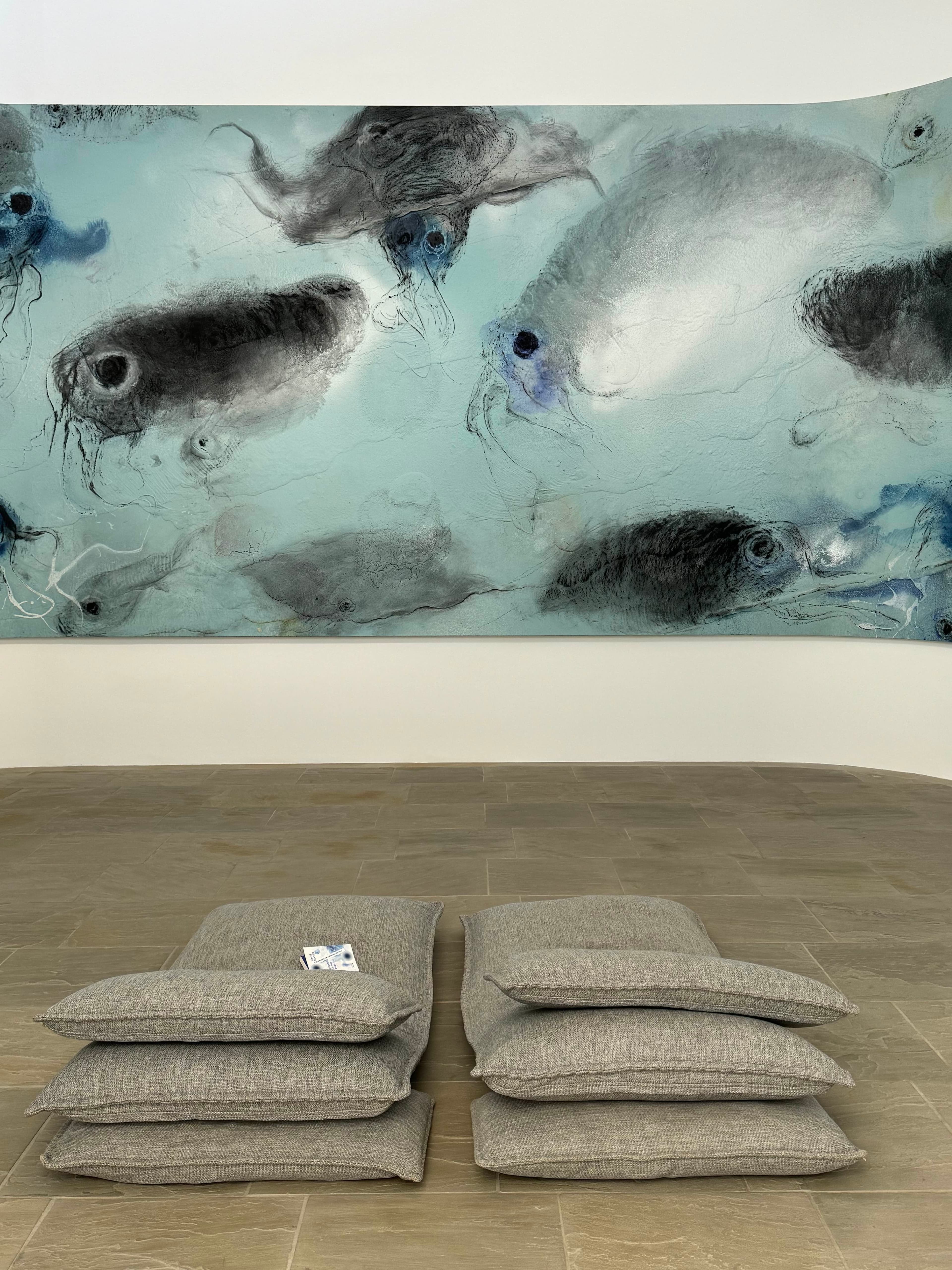 View of two cushions on the floor in a museum before a large blue-white painting of abstract sea creatures