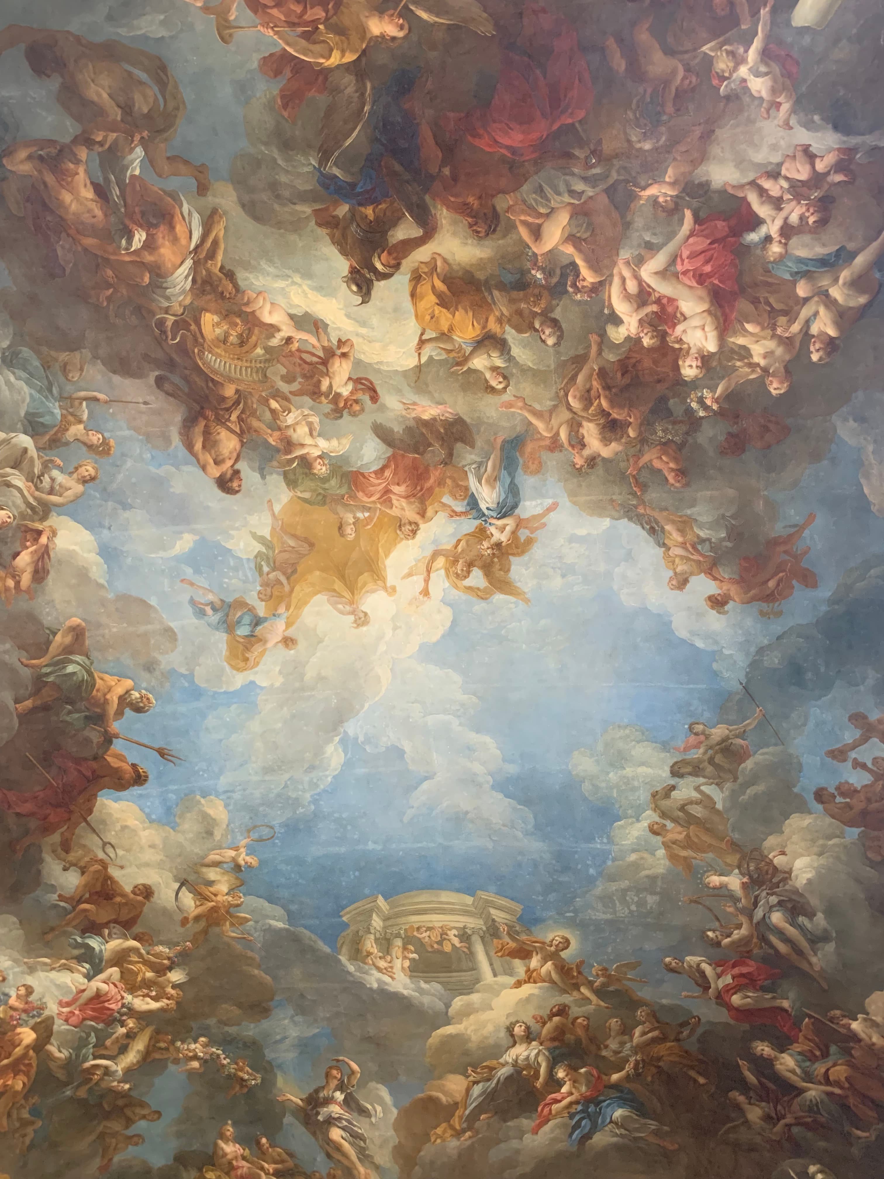 View of a beautifully ornate painted ceiling depicting a light blue cloudy sky with cherub-like figures