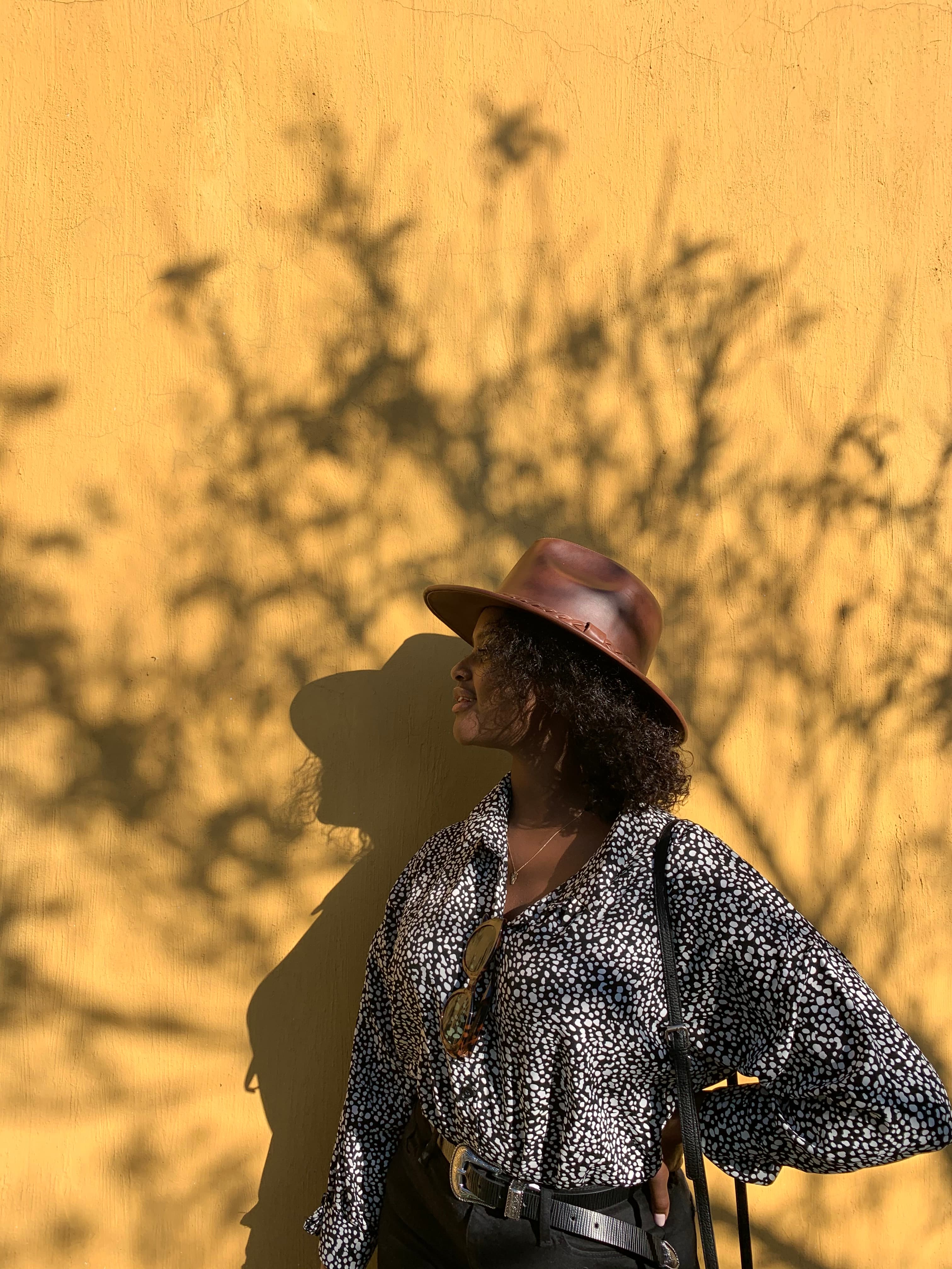 Advisor posing in silhouette against a bright yellow wall with the shadow of tree branches