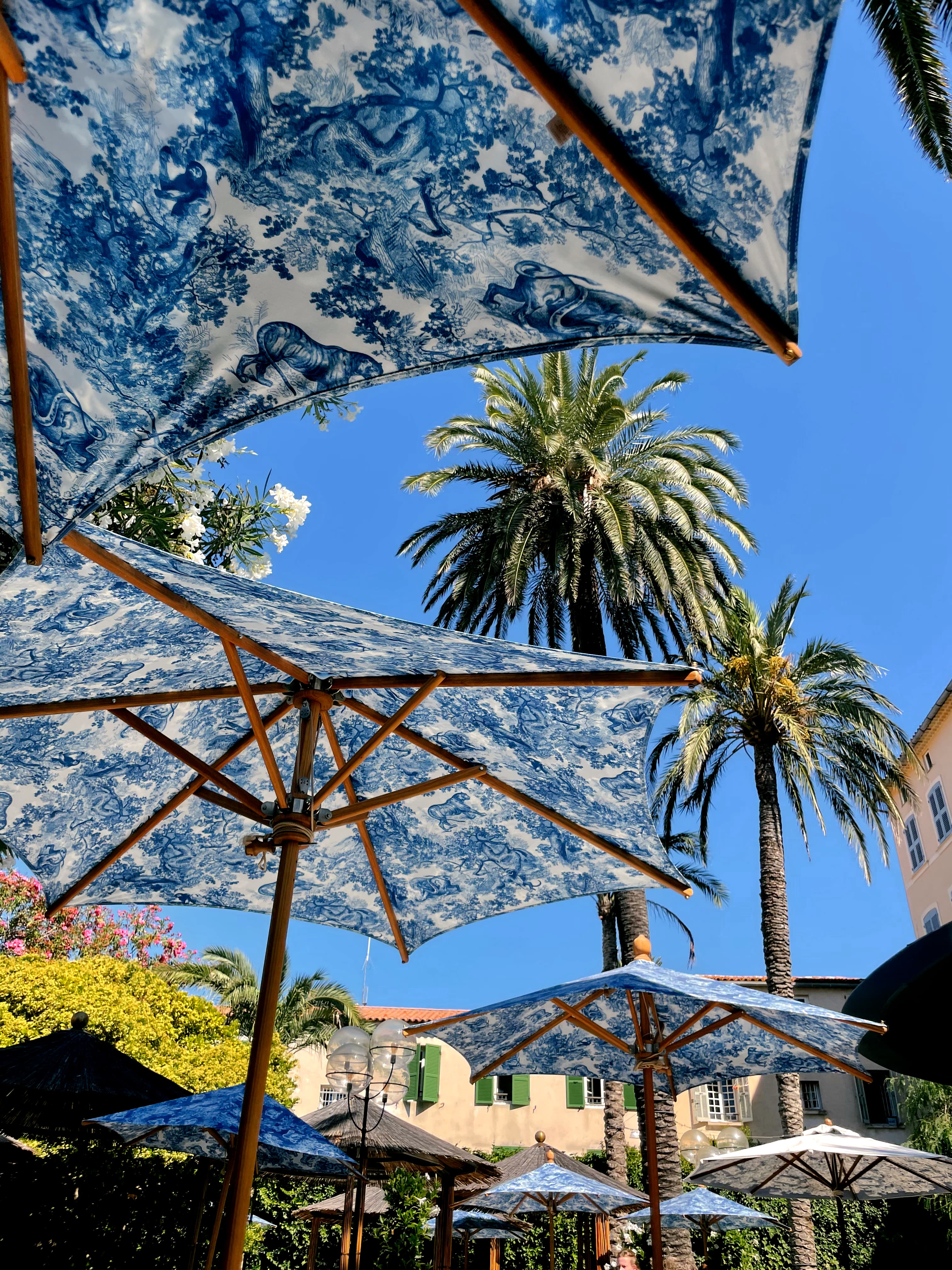 View of blue and white floral umbrellas and palm trees against a clear blue sky