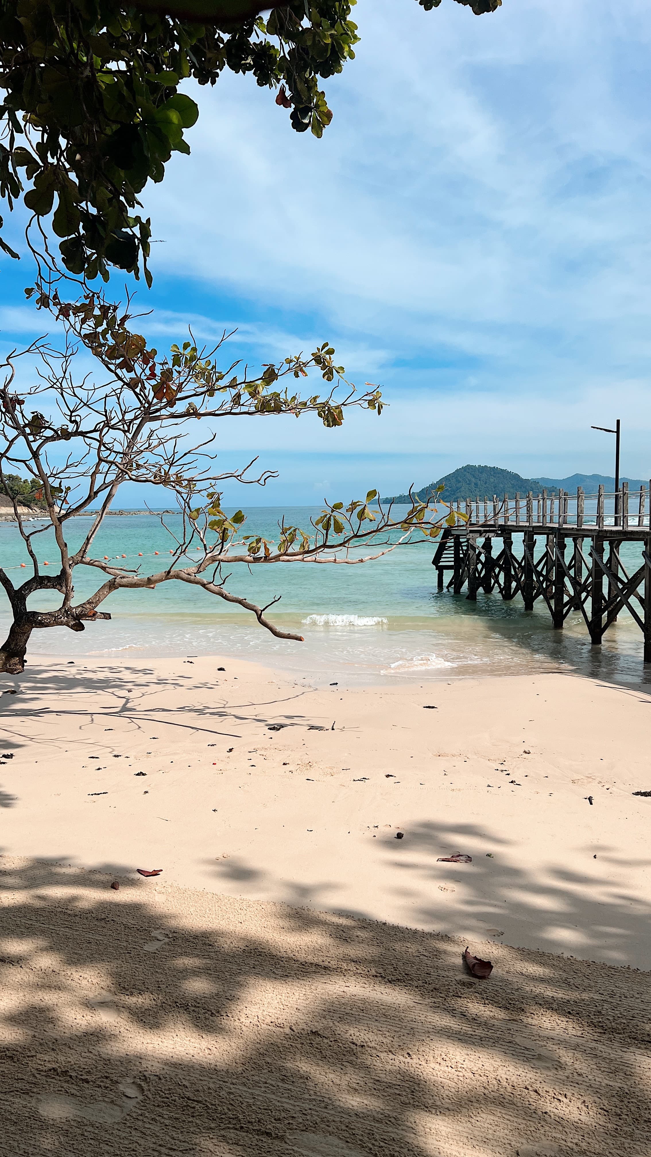 View of a beautiful white sand beach with a wooden pier extended out to calm seas