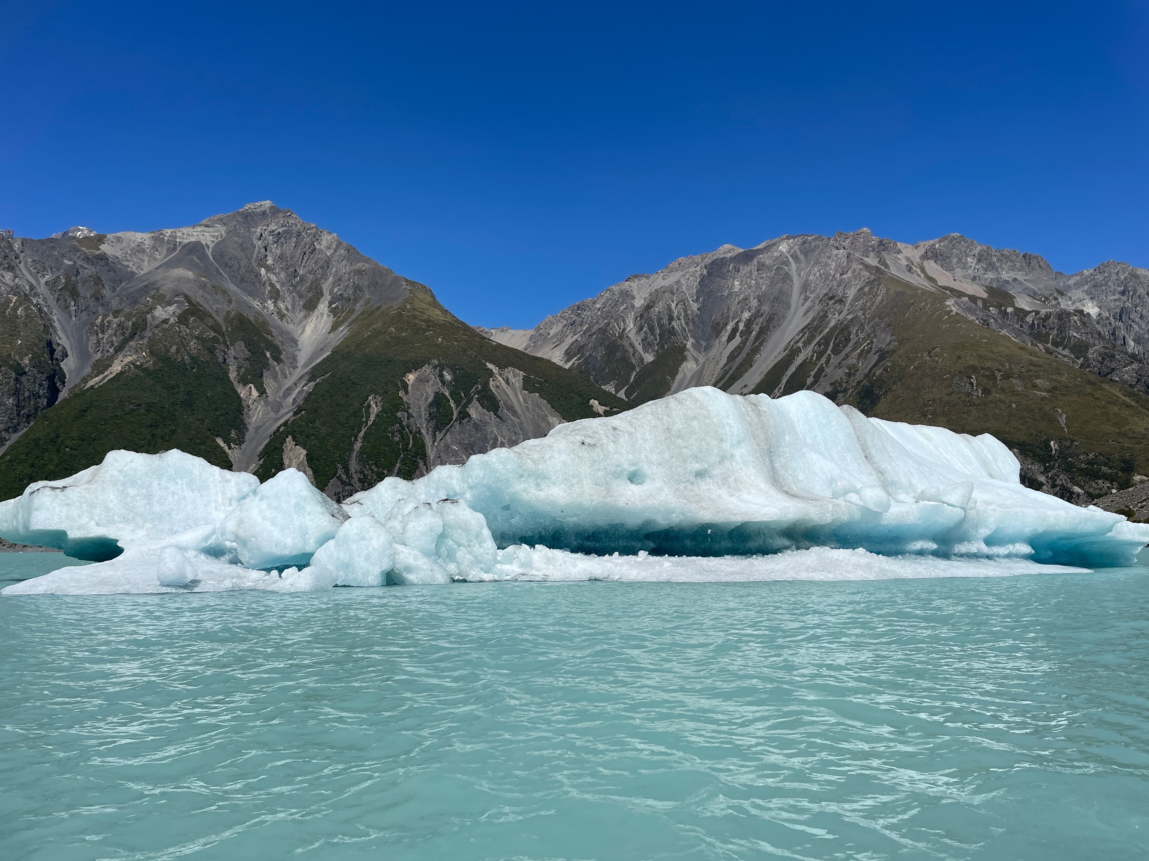 View of an iceberg in the ocean with mountains in the background.