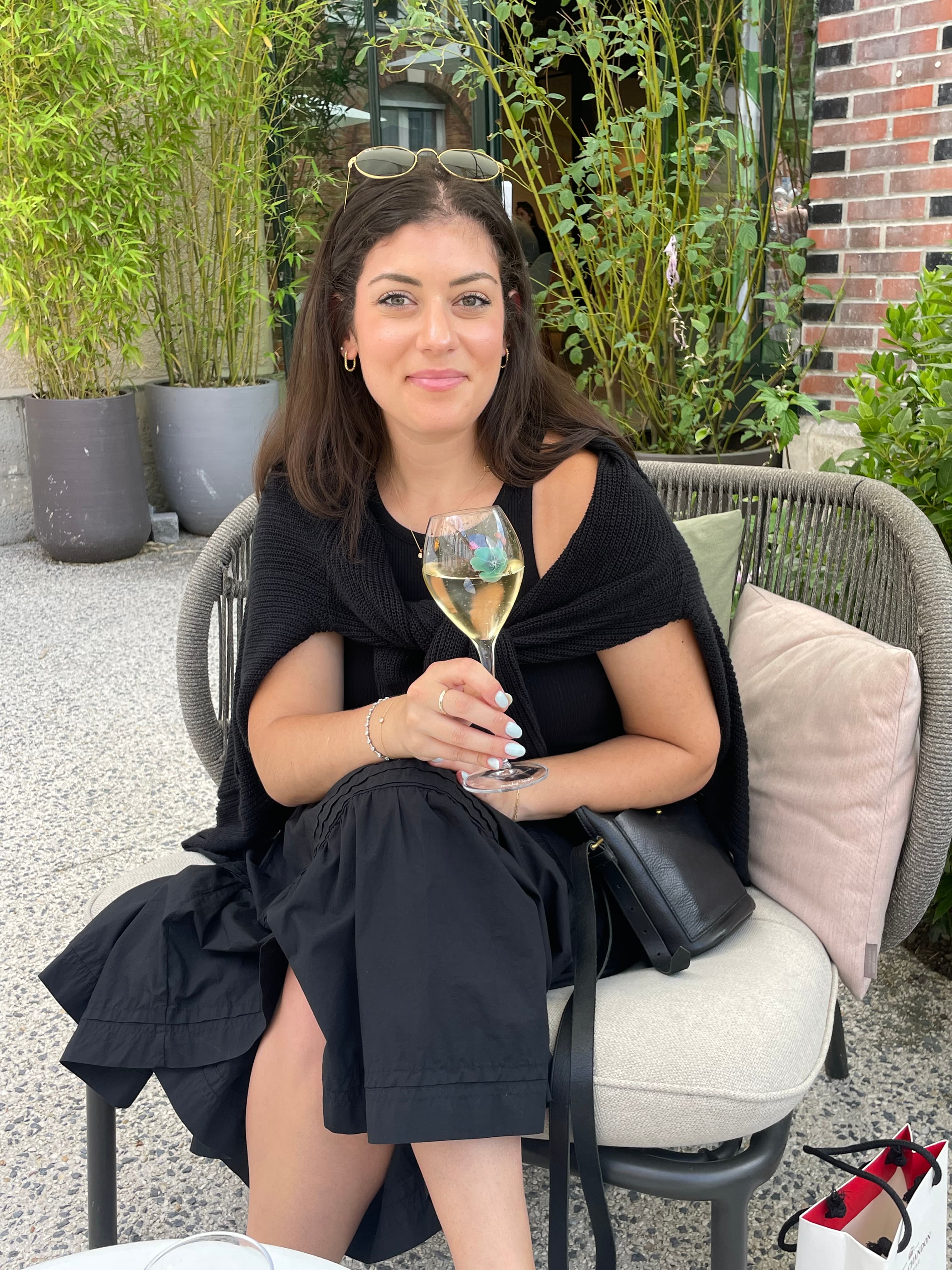 Jessica posing in a chair outdoors wearing an all black outfit holding a wine glass.