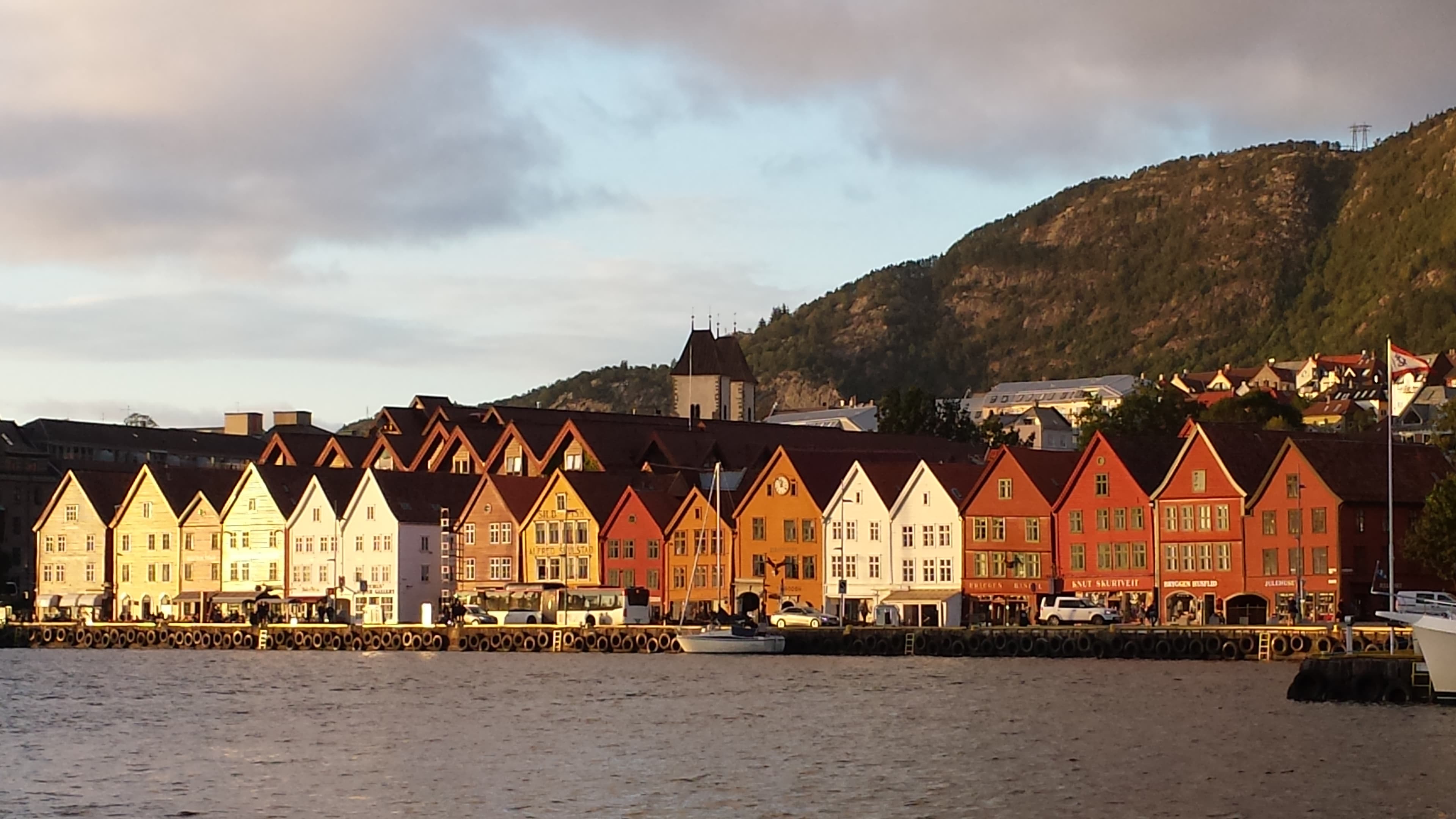 Row of buildings side by side by the water during the daytime with mountains in the background.