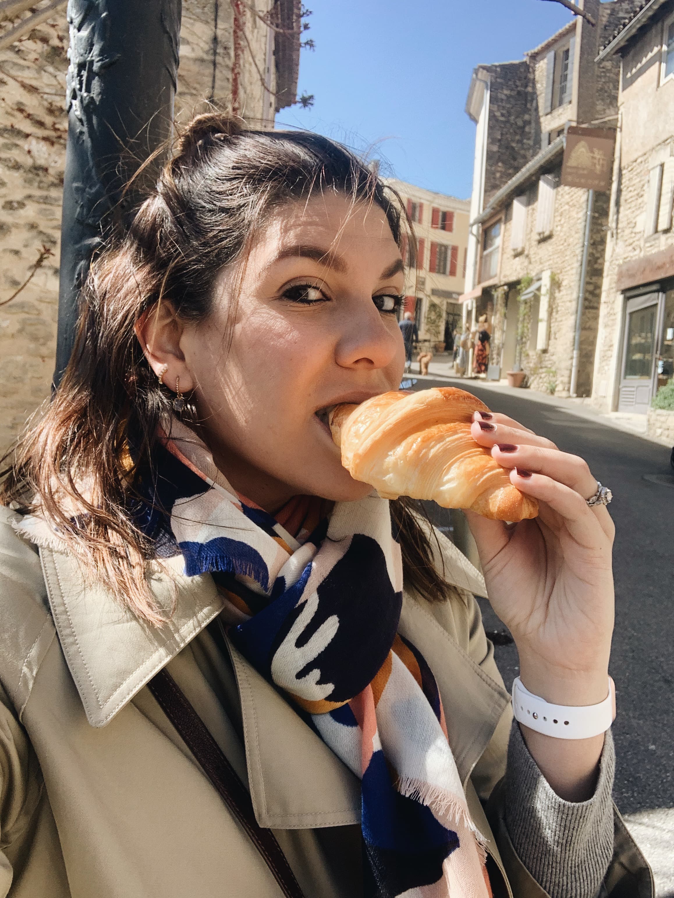 Ali eating a croissant outdoors during the daytime.