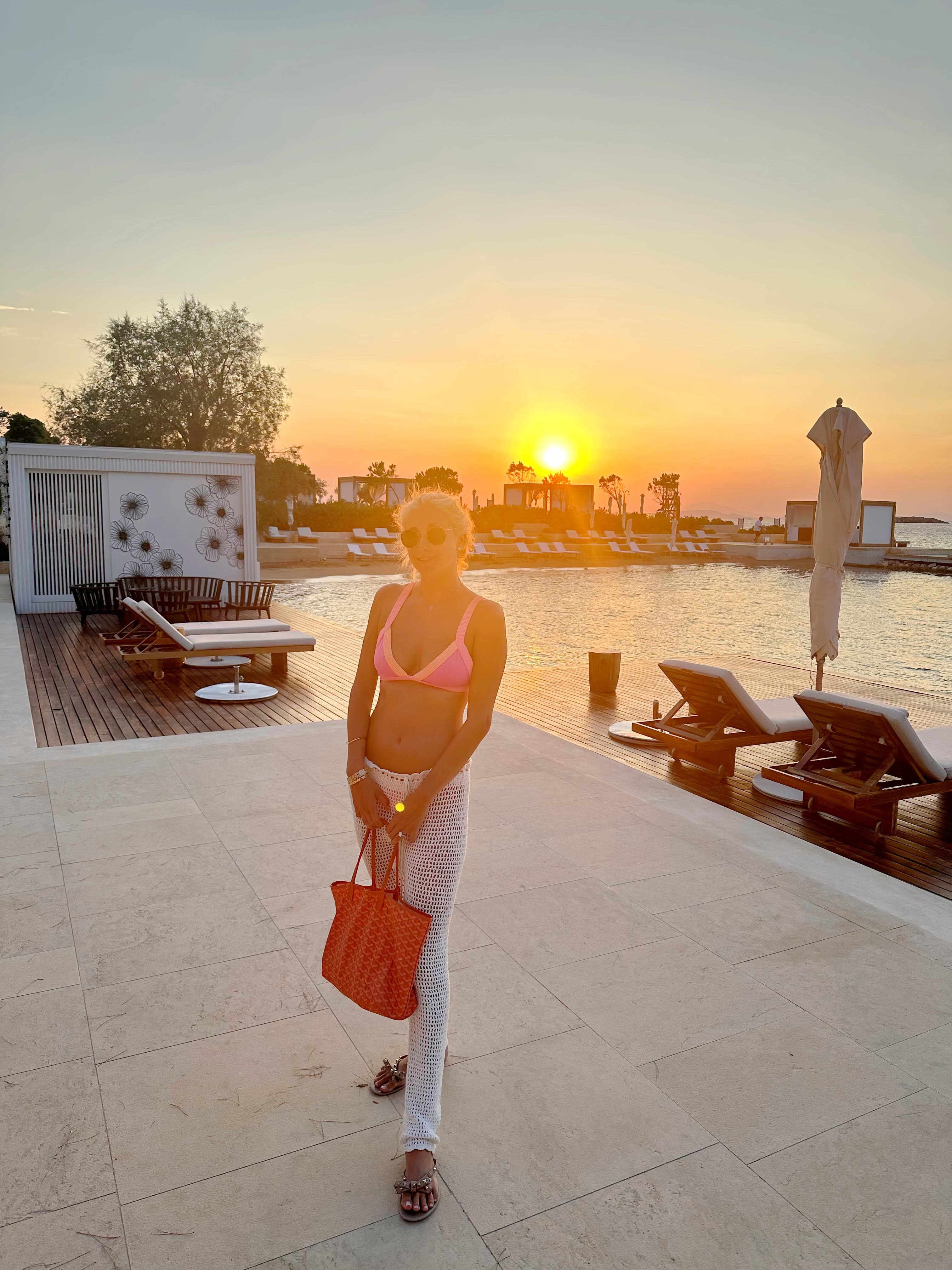 Advisor standing on a white platform in front of a calm body of water with the sun setting behind her.