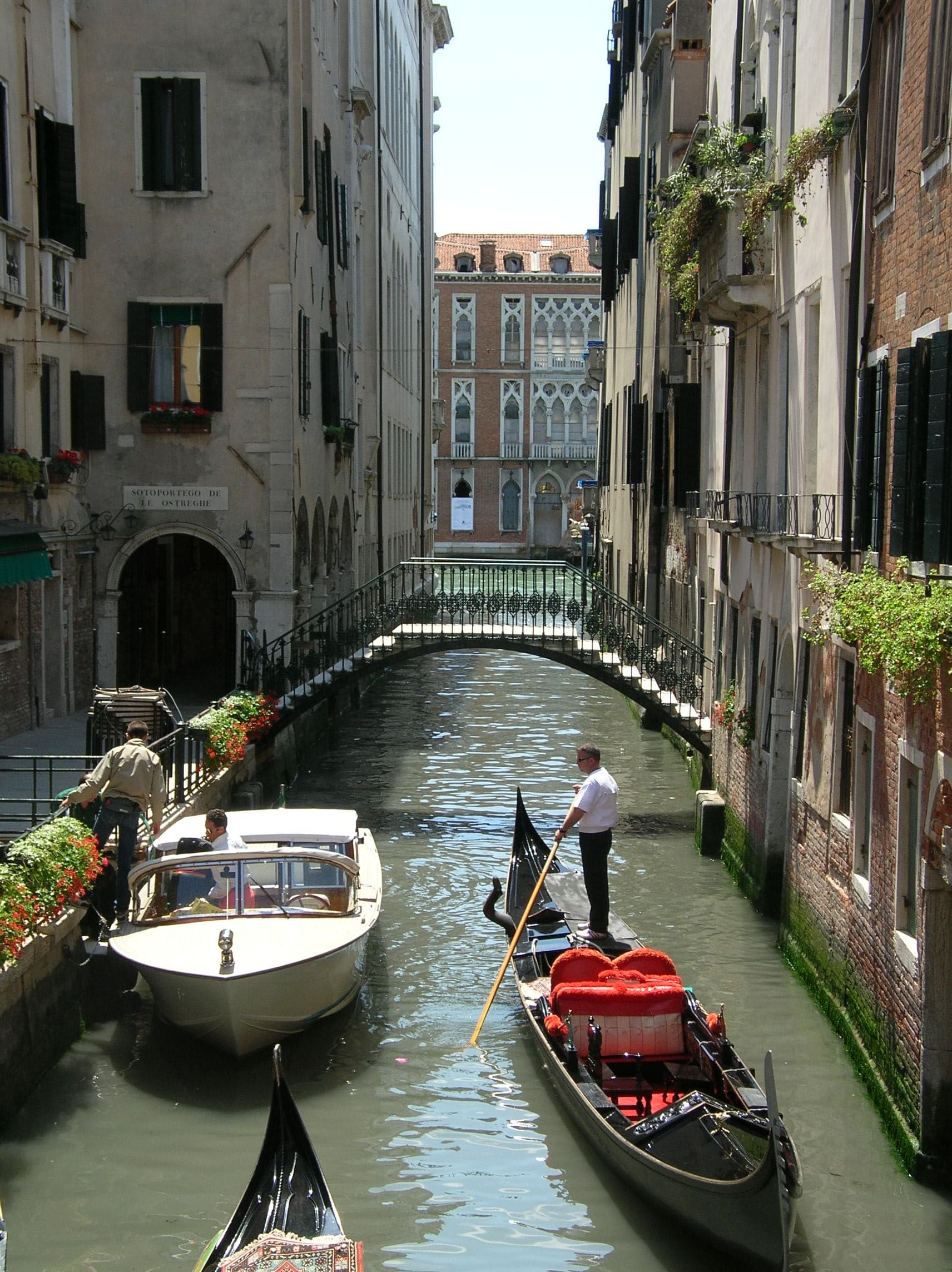 View of a Venice canal with a gondola and white boat floating beside each other on a sunny day