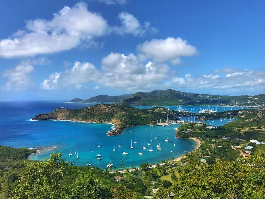 An aerial view of a tropical coastal town with sail boats along the coast line with a lush green forest and mountains.