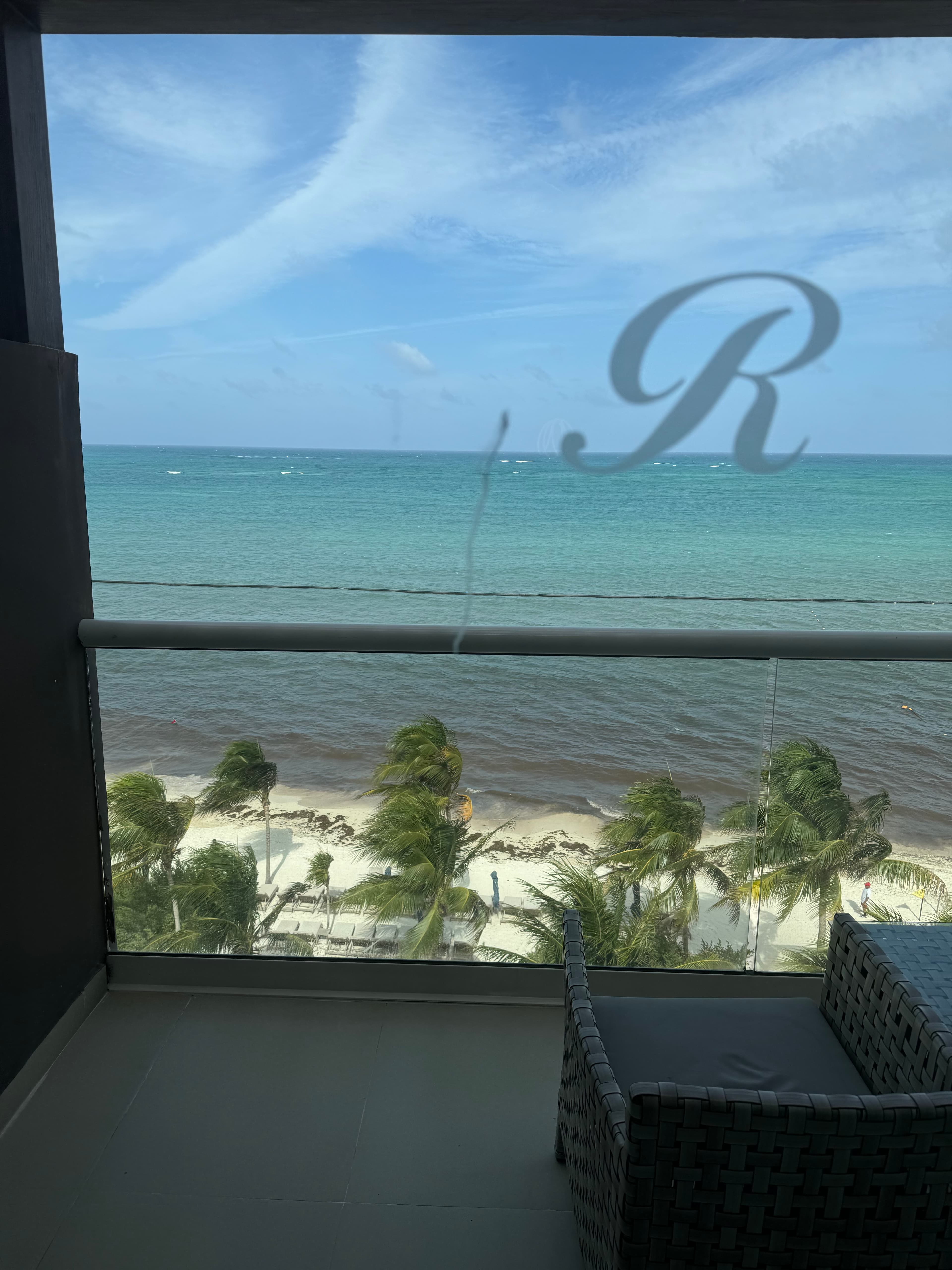 A view overlooking a white sand beach with palm trees and a calm ocean on a partly cloudy day.
