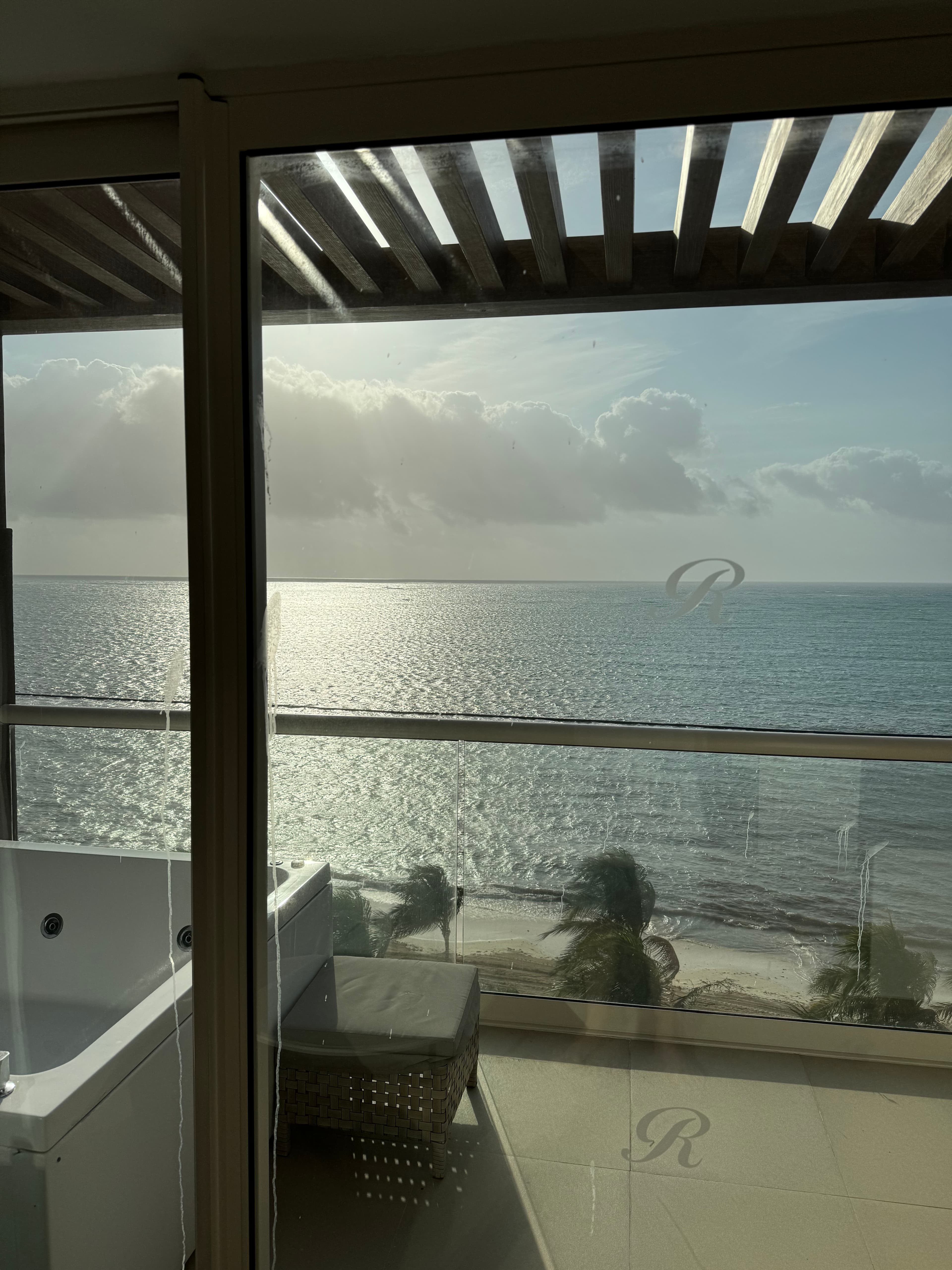A view looking off of a balcony with a spa at a calm ocean with the sun shining.