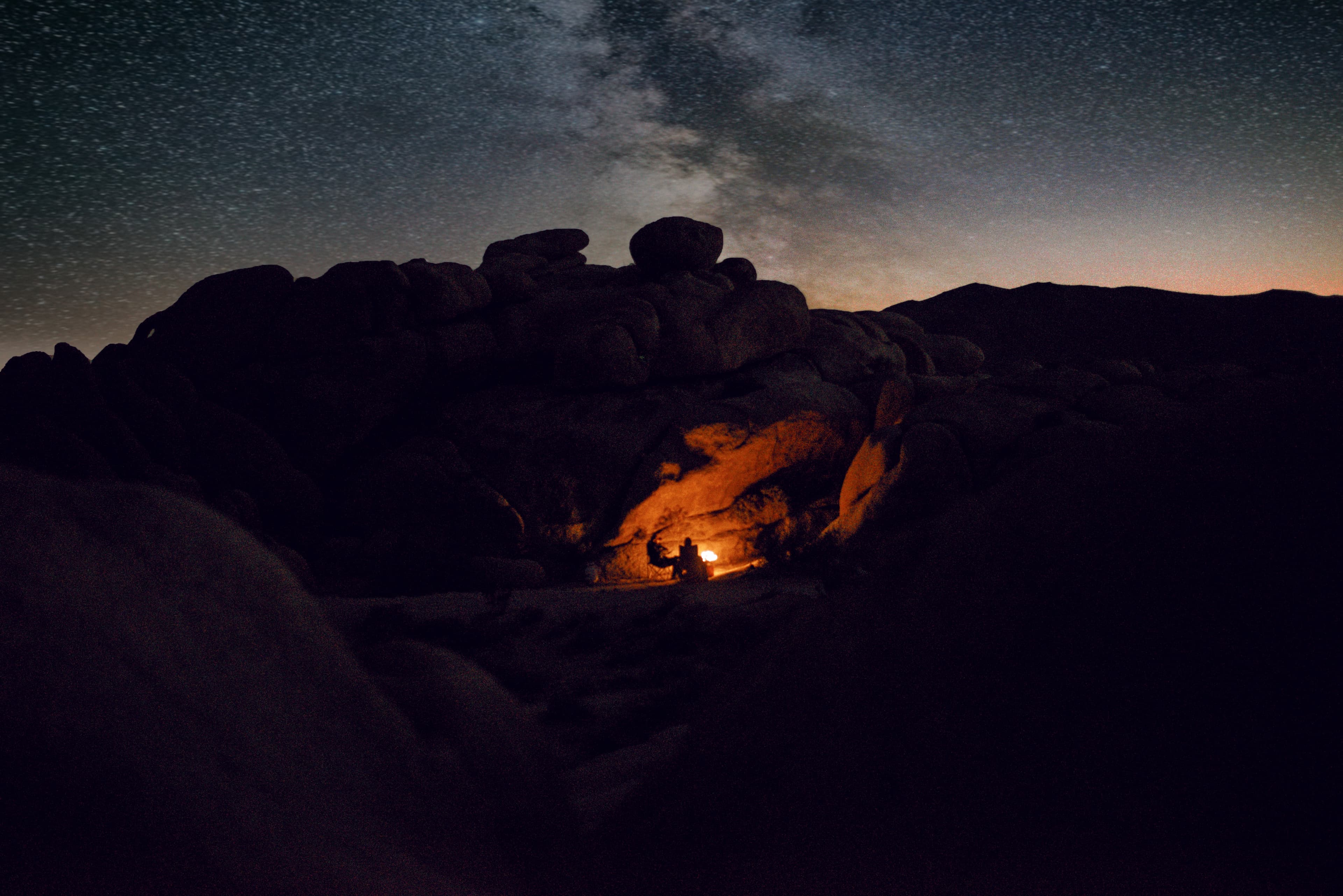 View of a small fire lit inside a cave under a starry sky