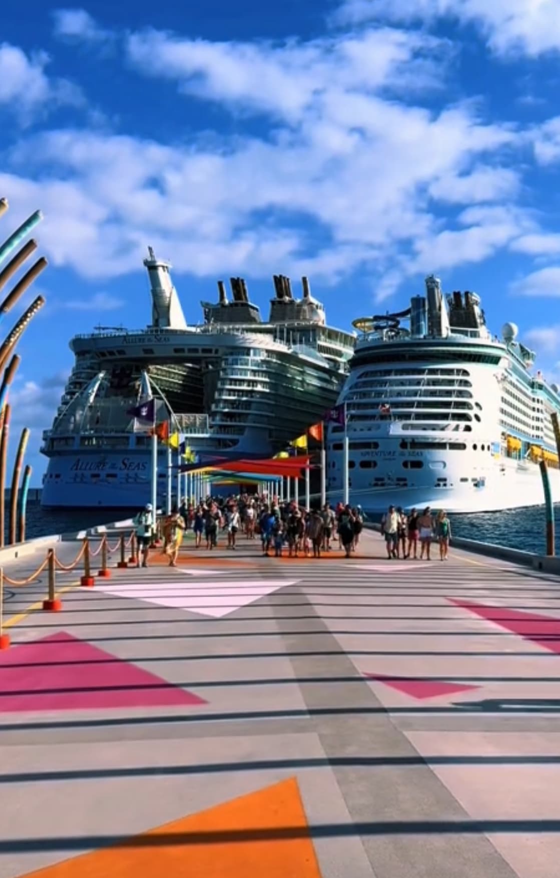 A view of two large cruise ships at the end of a dock that has a mural of colorful triangles painted on it during the day.