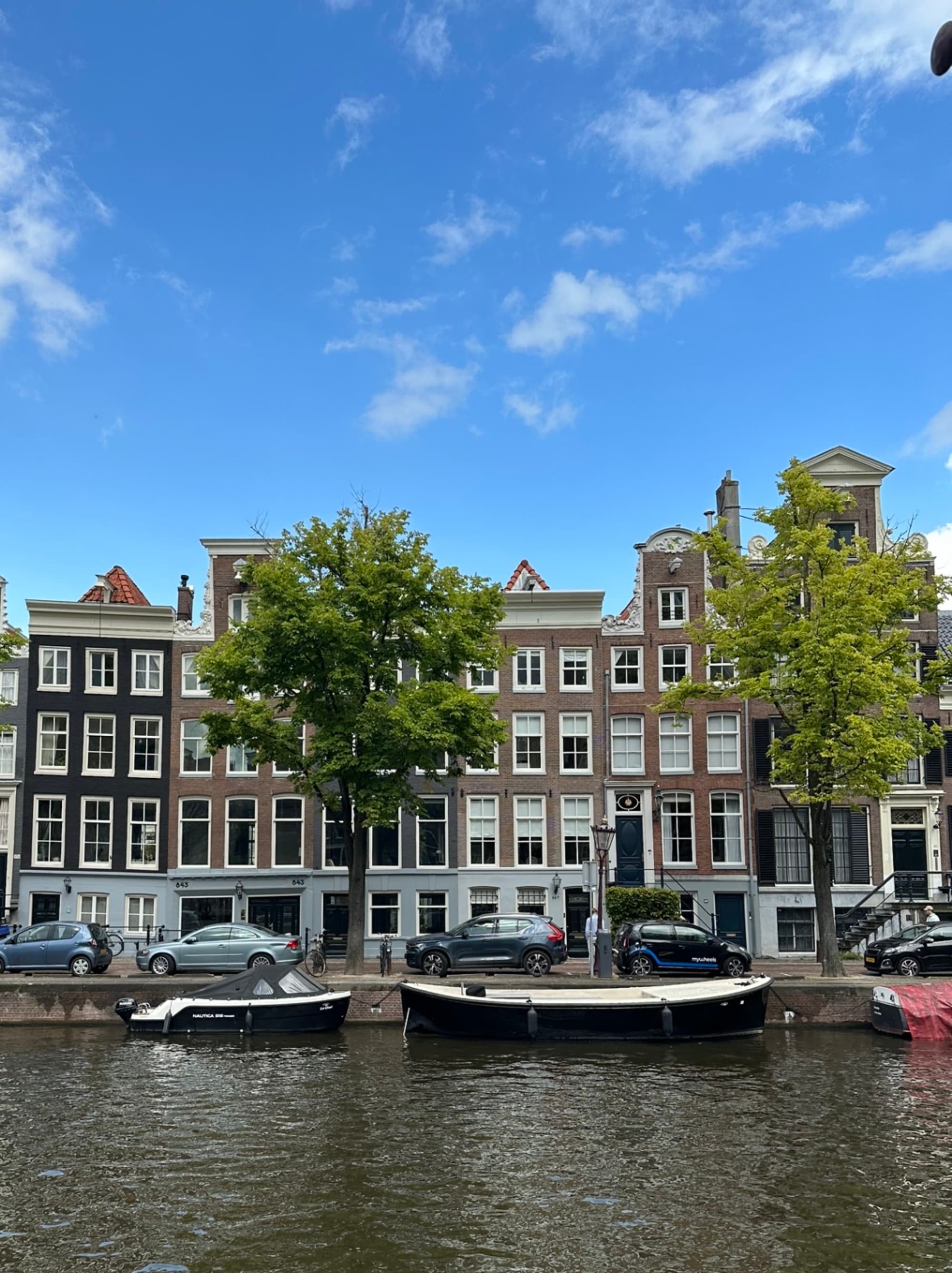 A row of traditional Dutch houses by a canal with boats and cars under a clear blue sky.