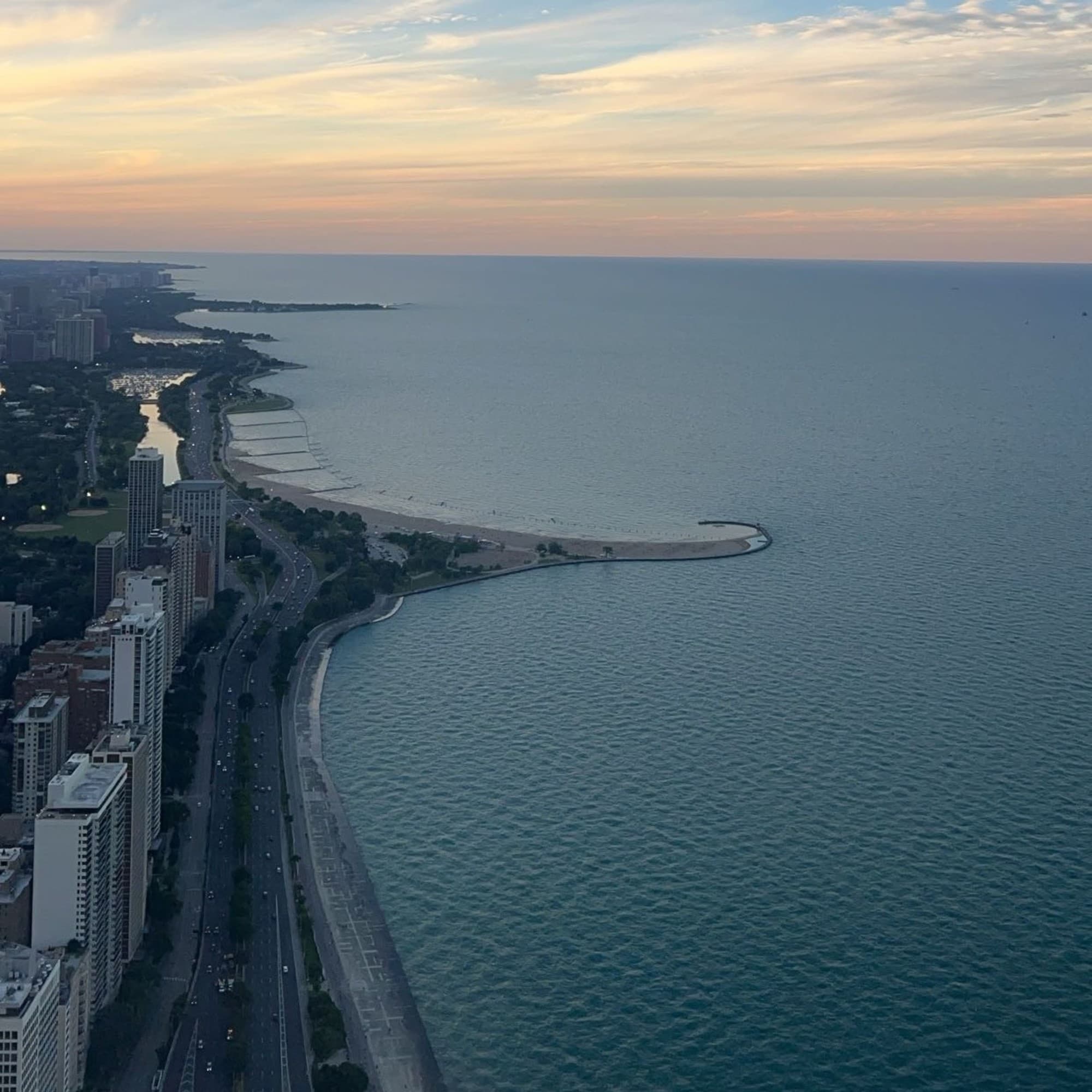 An aerial view of a coastal cityscape during twilight showcases the shoreline, buildings, and a road alongside the beach.