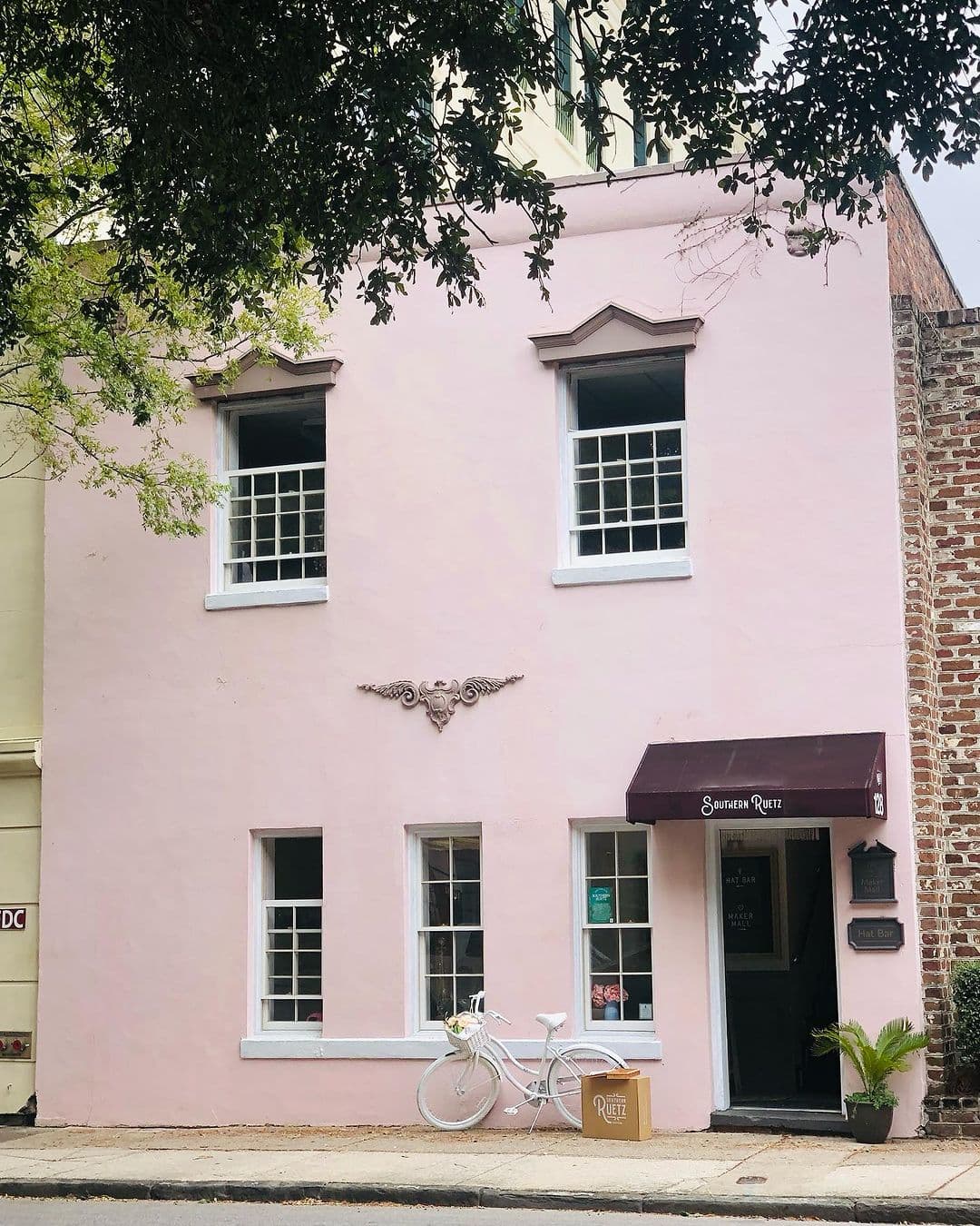 A brick building, with a pink storefront, and a white vintage-style bicycle outside of it.