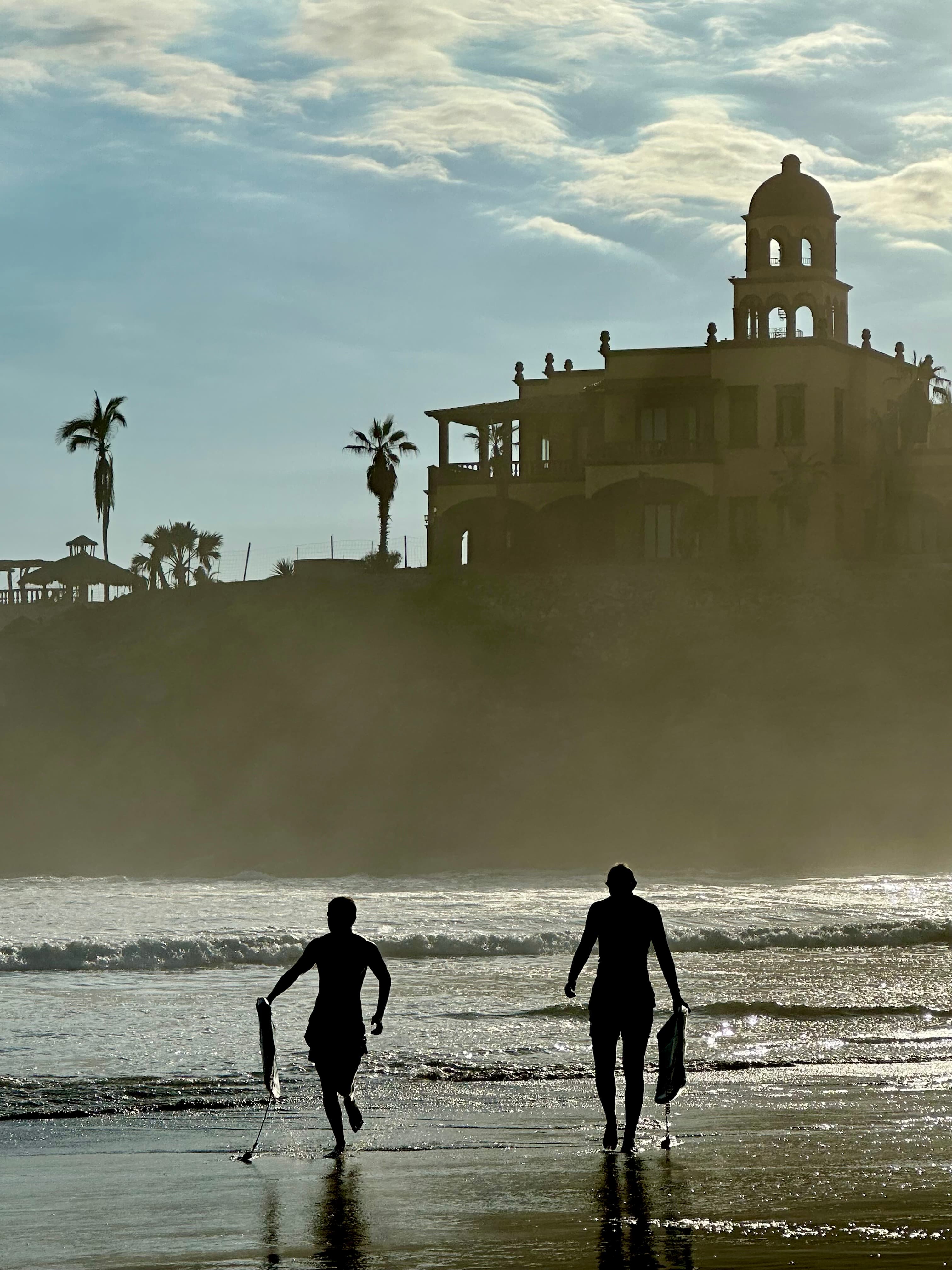 Two people running on the beach running toward the water holding surfboards