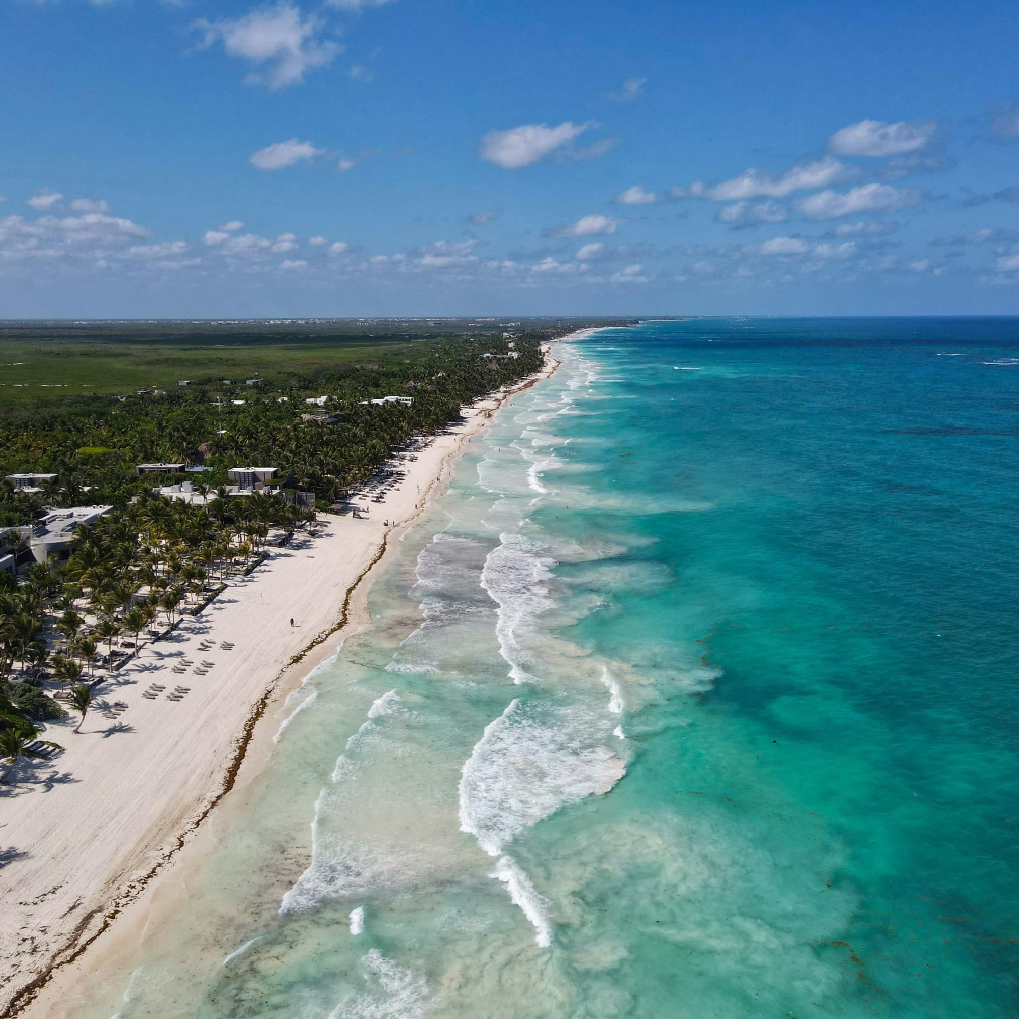 Aerial view of a tropical beach with clear turquoise waters, white sands, and dense greenery.