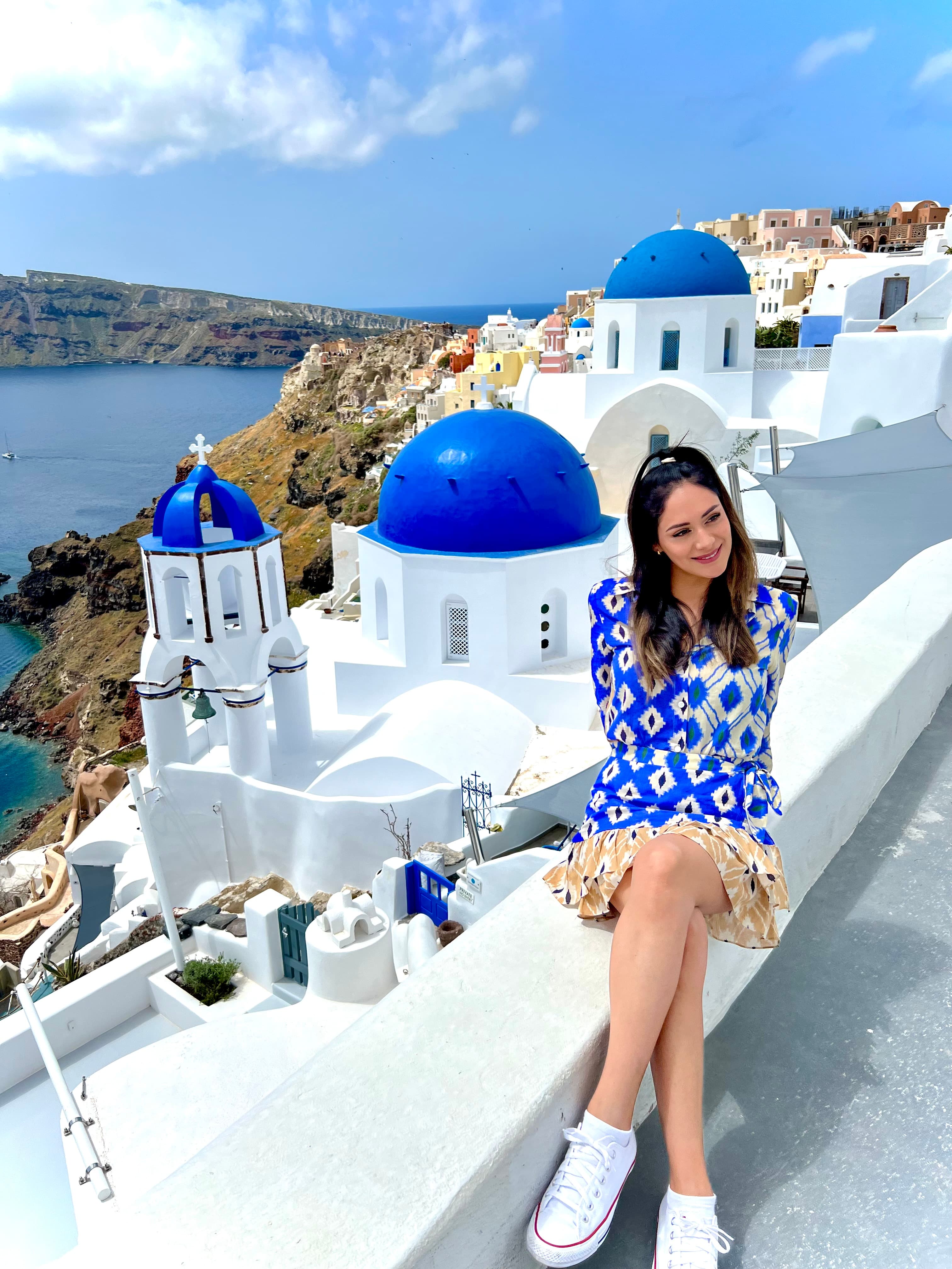 Advisor in a blue and white dress sitting on a white ledge overlooking the white buildings of sunny Santorini