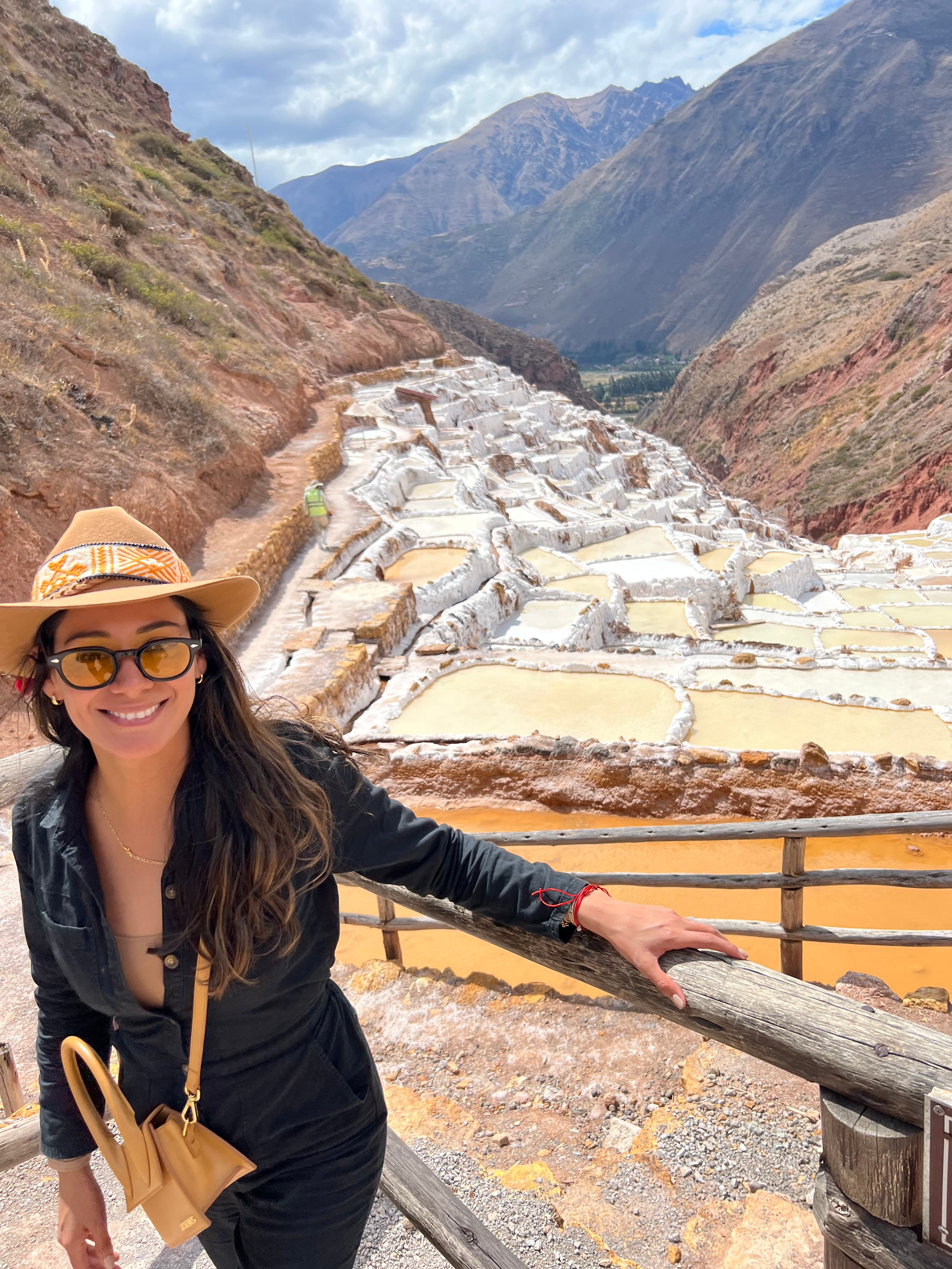 Advisor smiling on a wooden staircase overlooking an ancient archaeological site in a sunny mountain range