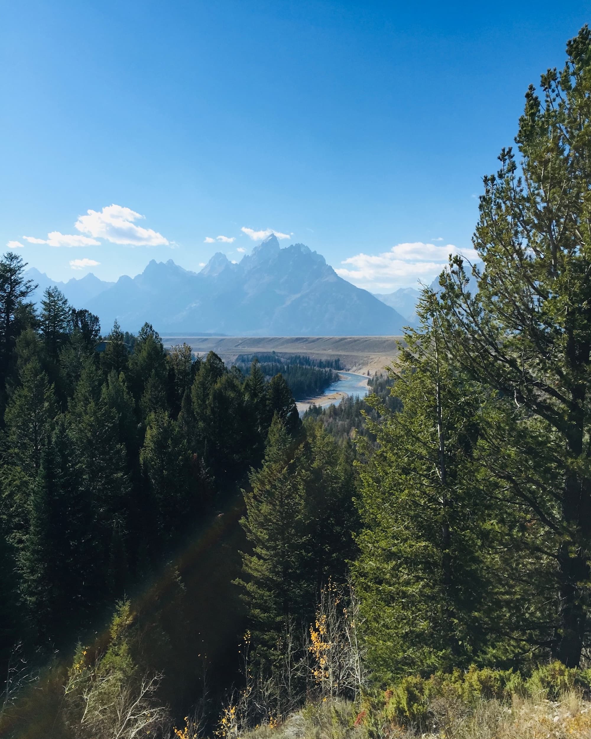 A picturesque mountain range with a river and dense forests in the foreground.