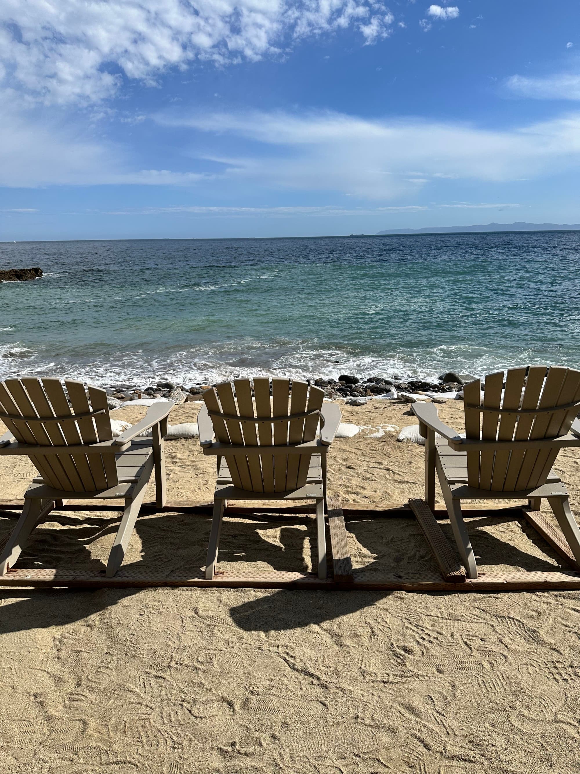 Three lounge chairs sitting on a beach in front of the water during daytime