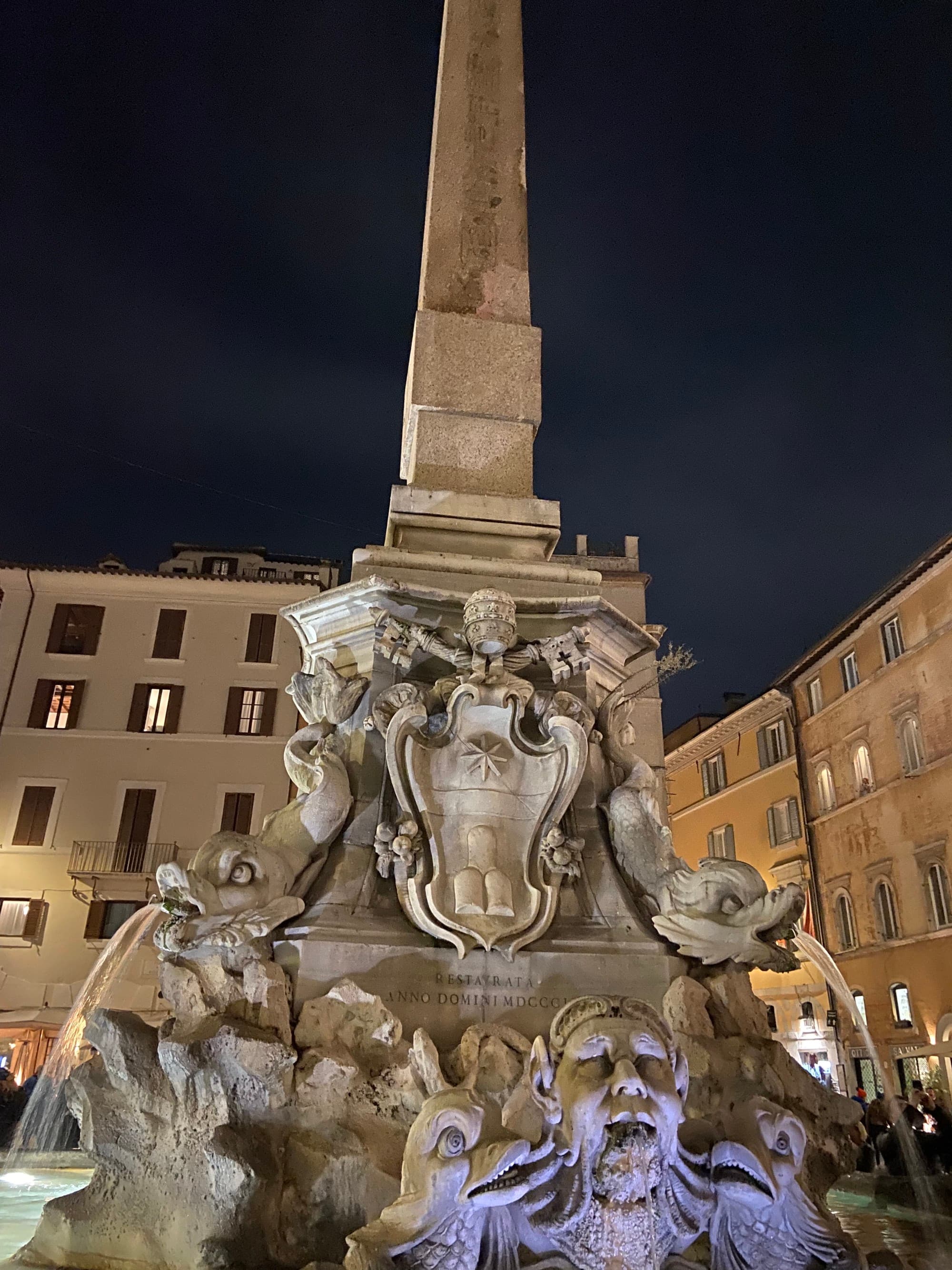 A landmark fountain in the center of a piazza at night,