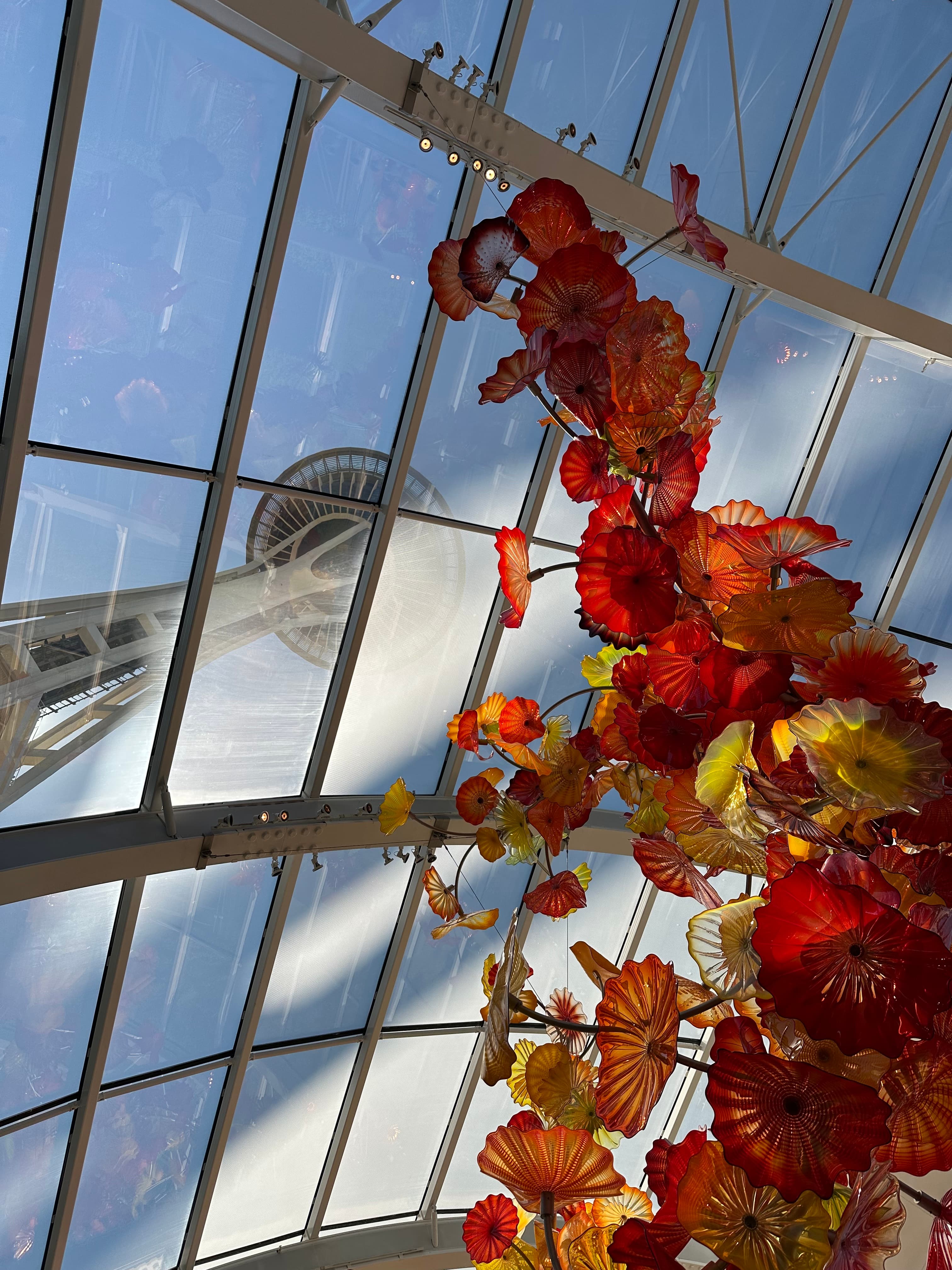 Enormous orange and red blown glass sculpture underneath a glass ceiling with a view of the Space Needle above.