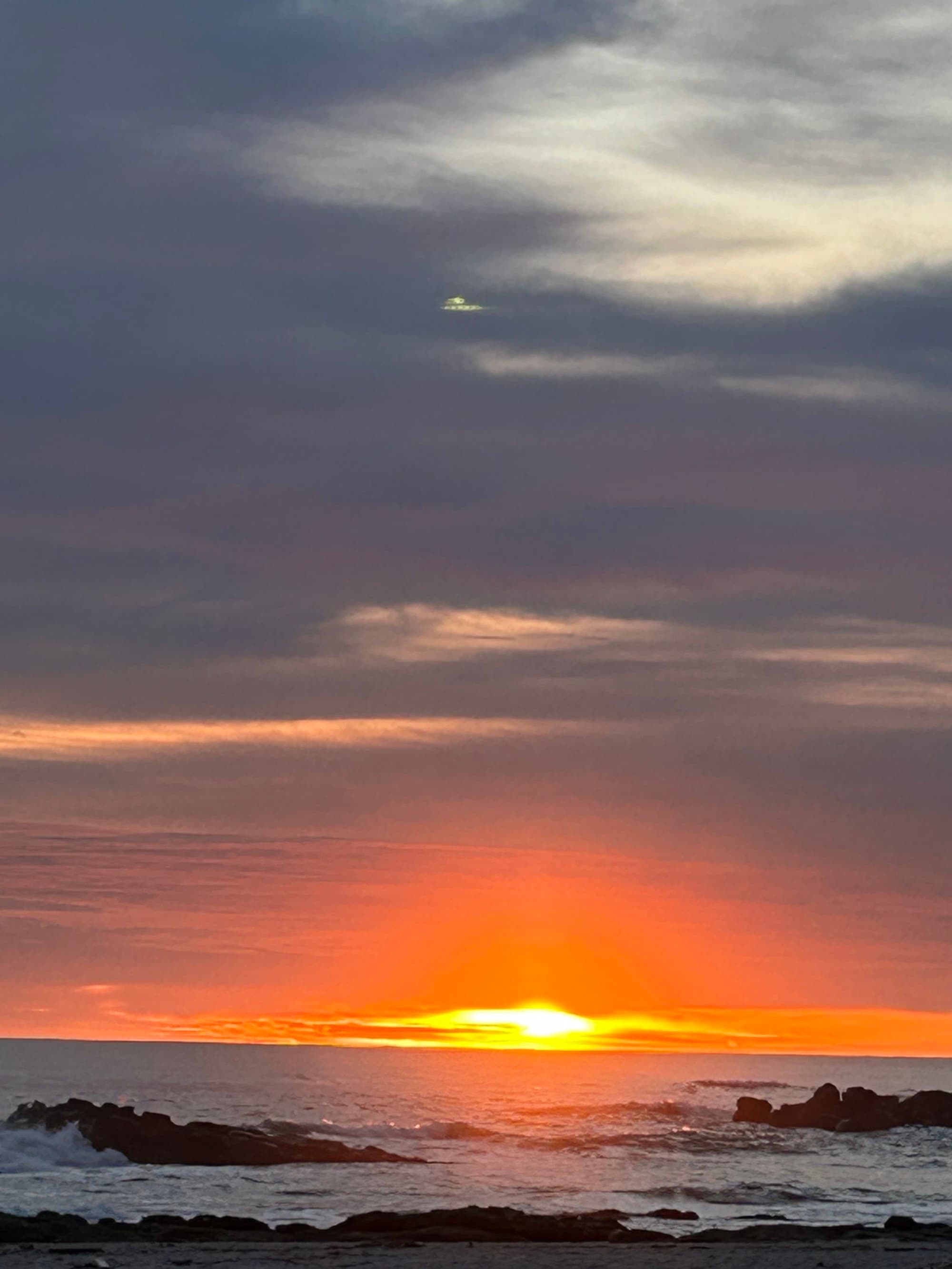 A sunset over the ocean with the sun partially obscured by the horizon and clouds, creates a vibrant display of colors in the sky.