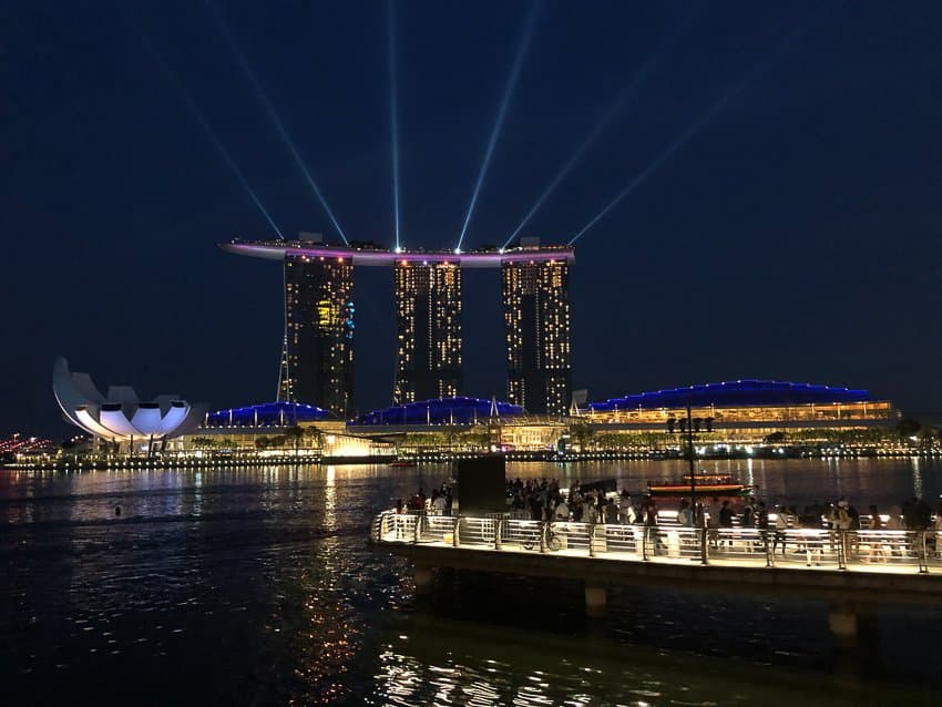 A city on the water at night with light beams shining in the sky