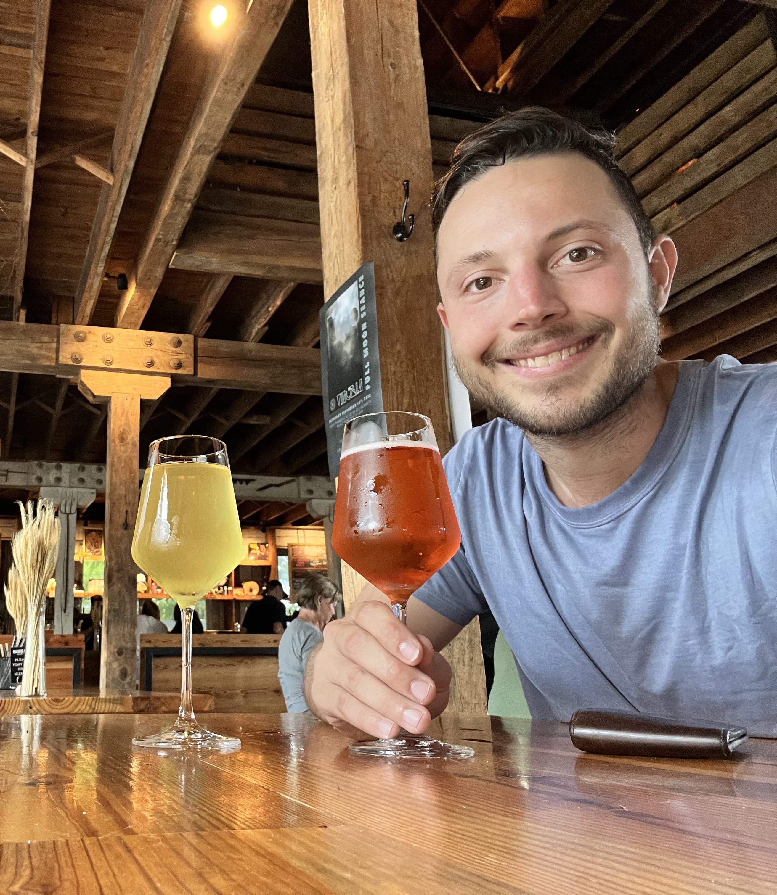 Steven Lawrence taking a selfie with two beers at a wooden bar at AVL Forestry Camp