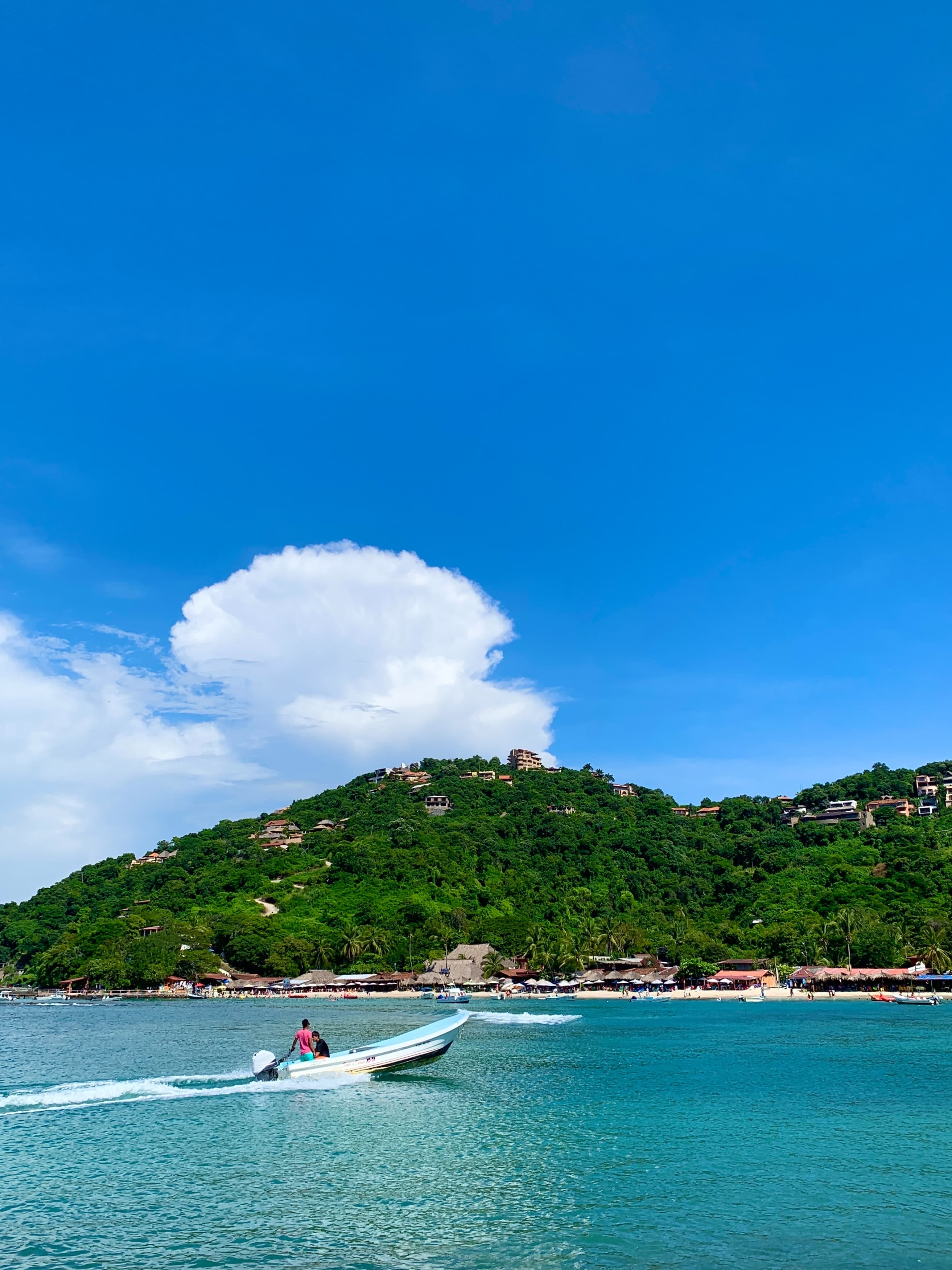 small boat cruising through clear blue waters with island scene in the background