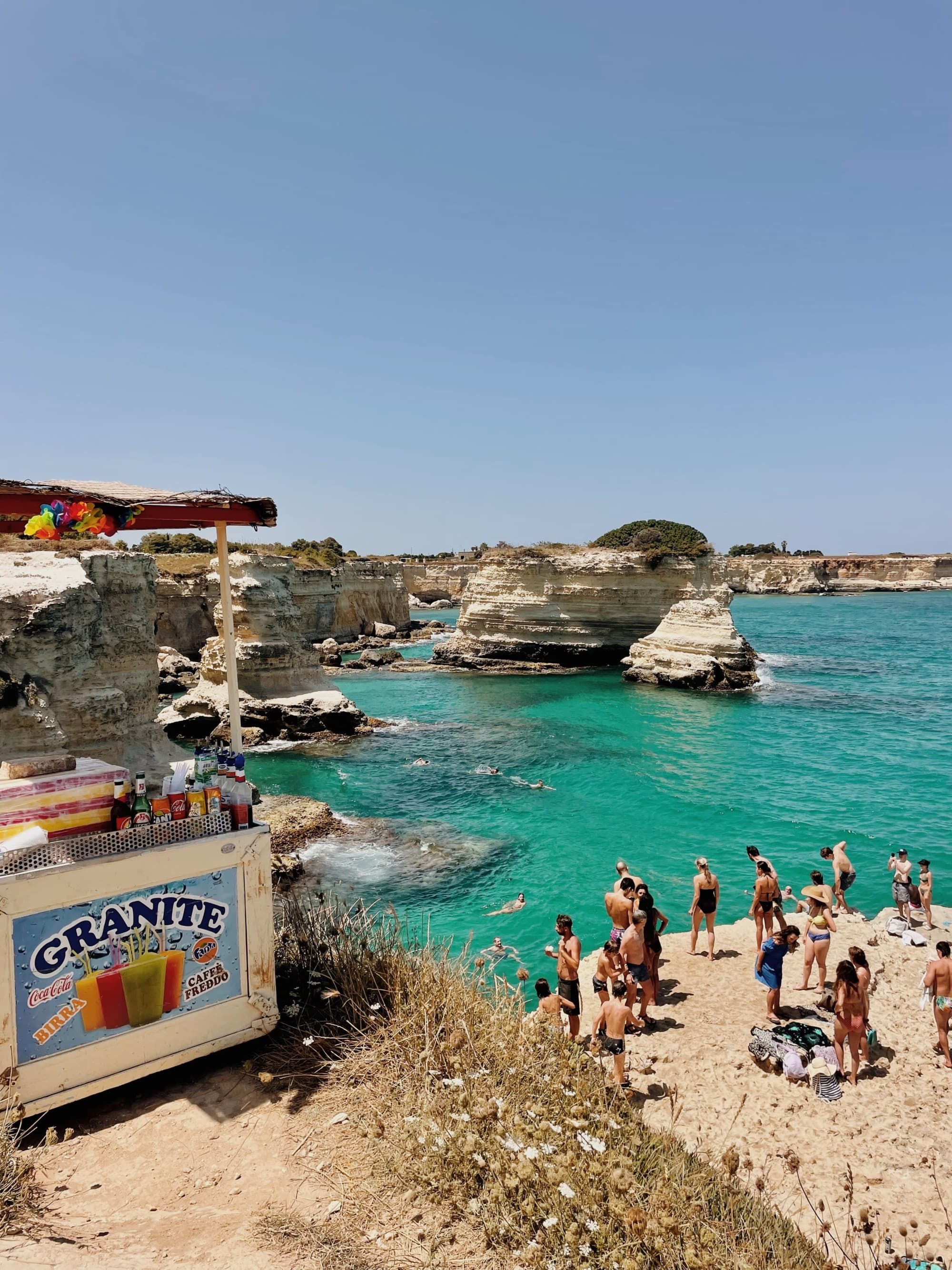 An aerial view of the beach with people standing on shore during daytime.