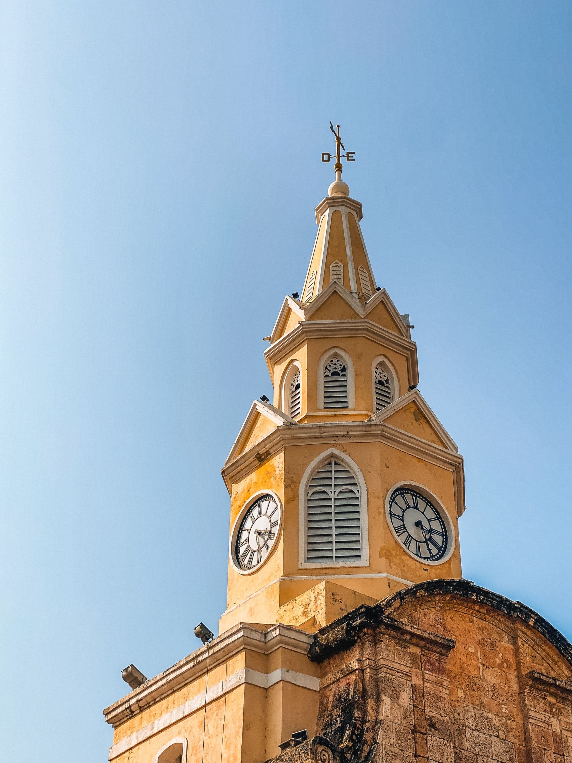 A tall yellow tower with a clock on top of it.