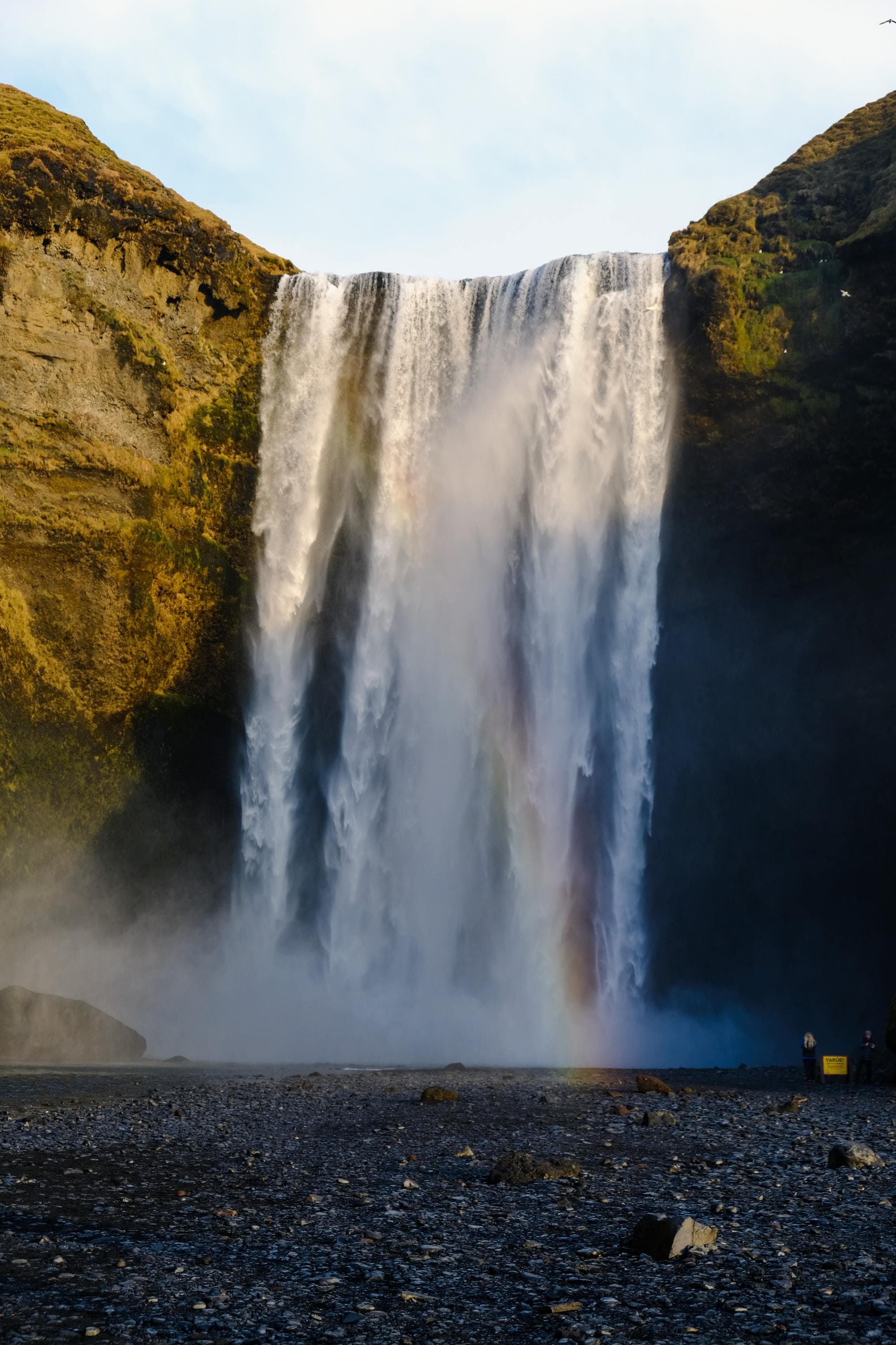 a waterfall onto black sand beach with a rainbow appearing from the pool below