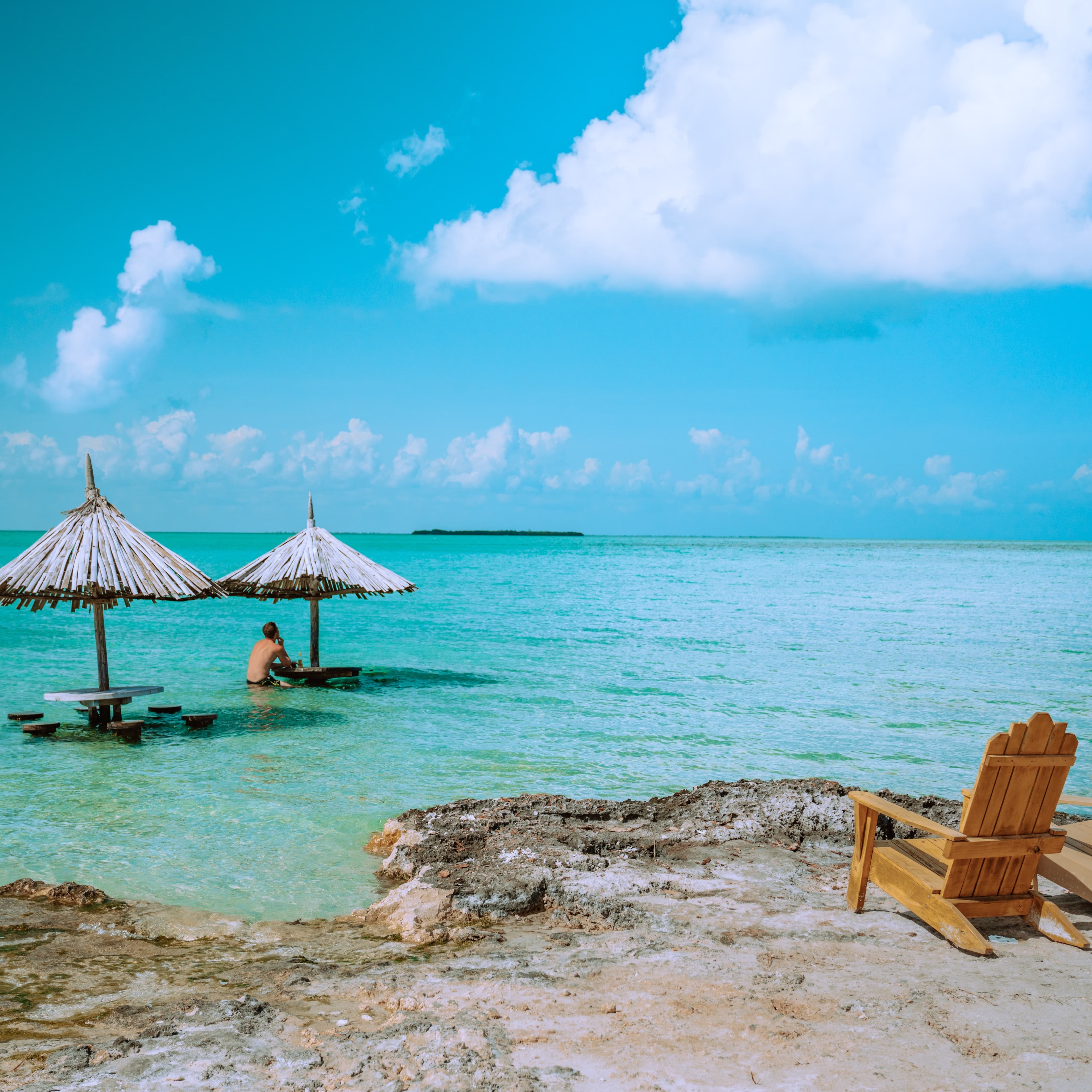 A beach view of Belize with wooden lounge chair and umbrella.