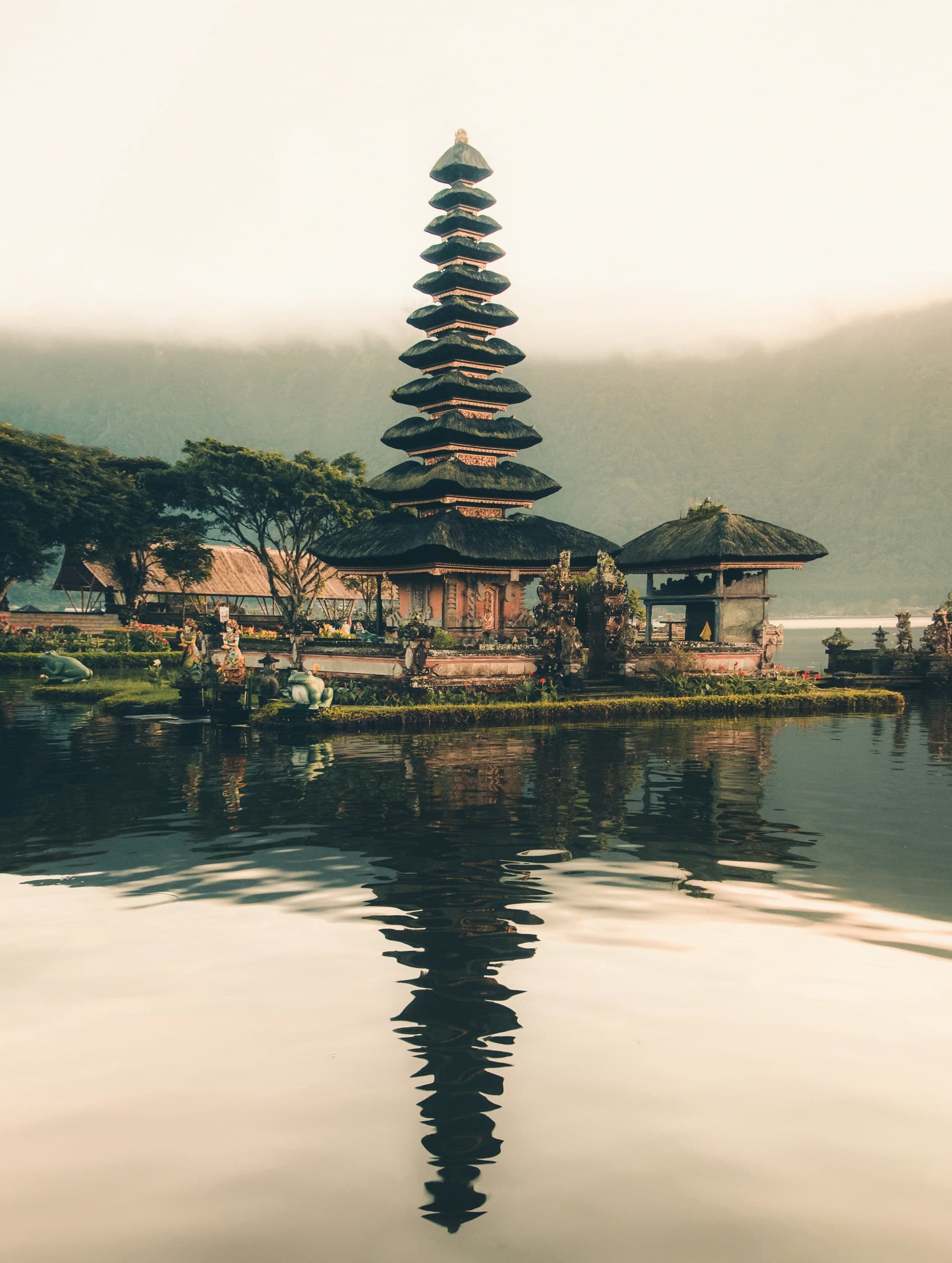 A picture of a temple beside a body of water and trees during daytime.