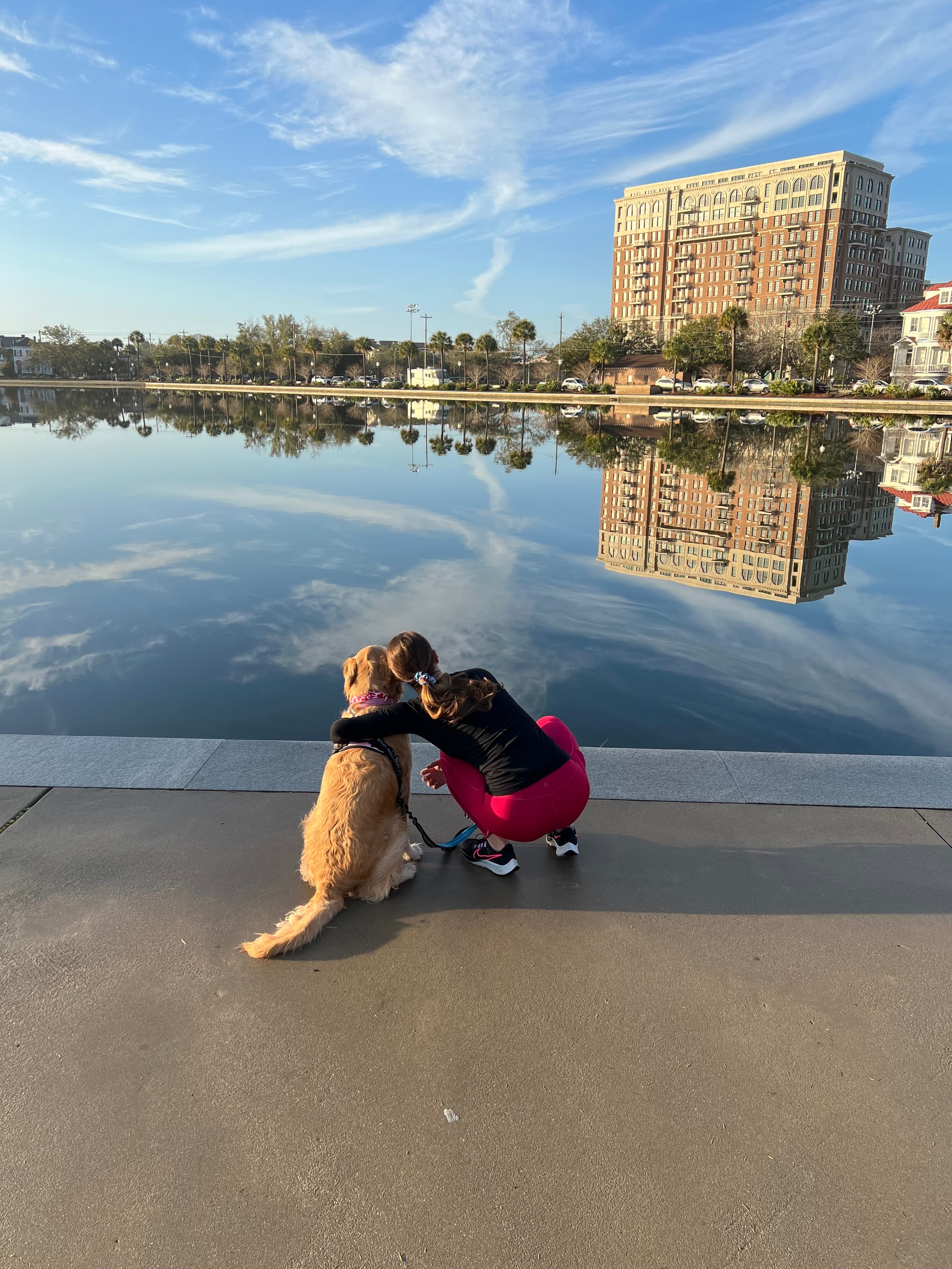 A person hugging a dog while looking out at a body of water