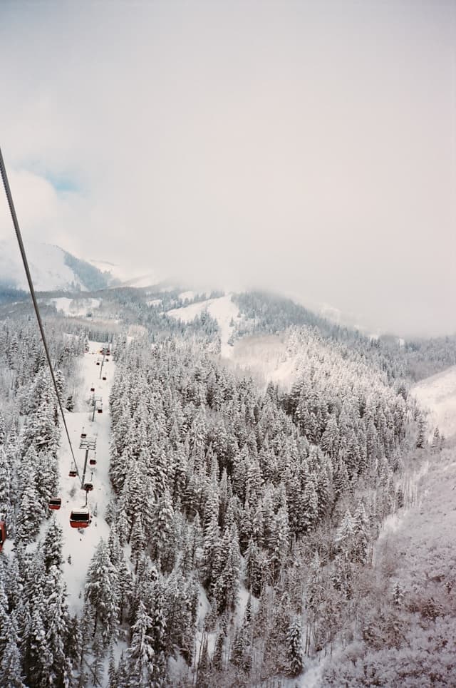 An overhead view of a ski lift above snow covered pine trees and mountains in Park City, Utah.