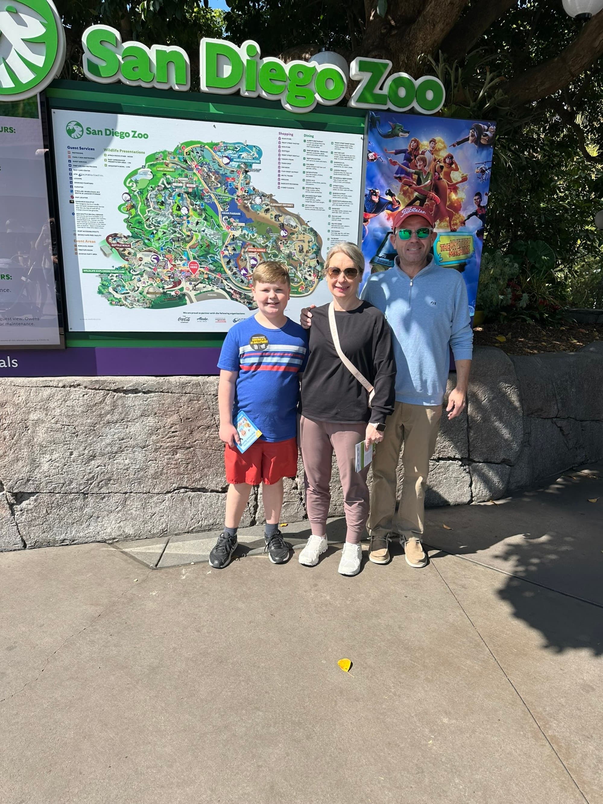 A picture of a family posing in front of the San Diego Zoo gate during the daytime.