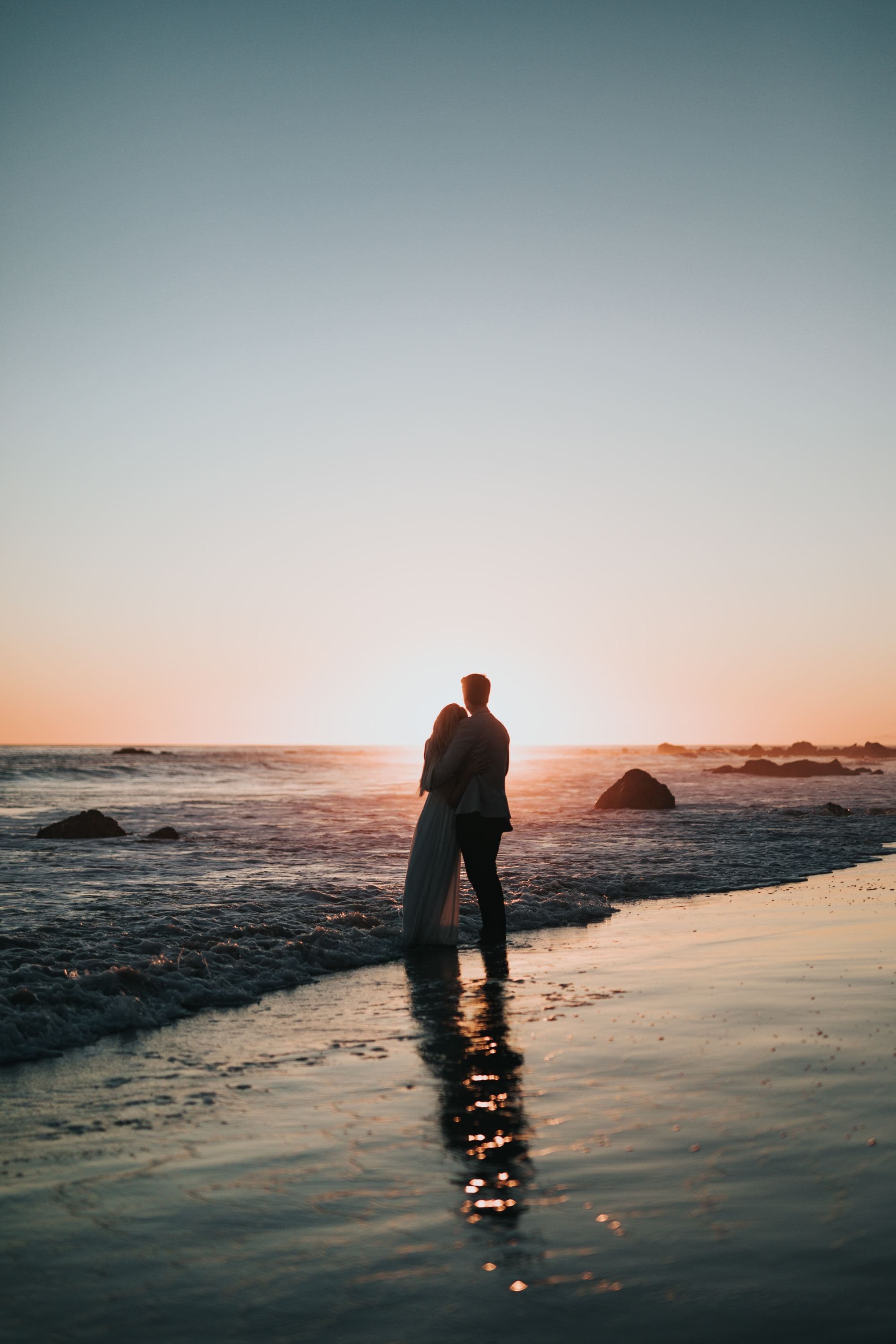 A couple standing near the beach during sunset.