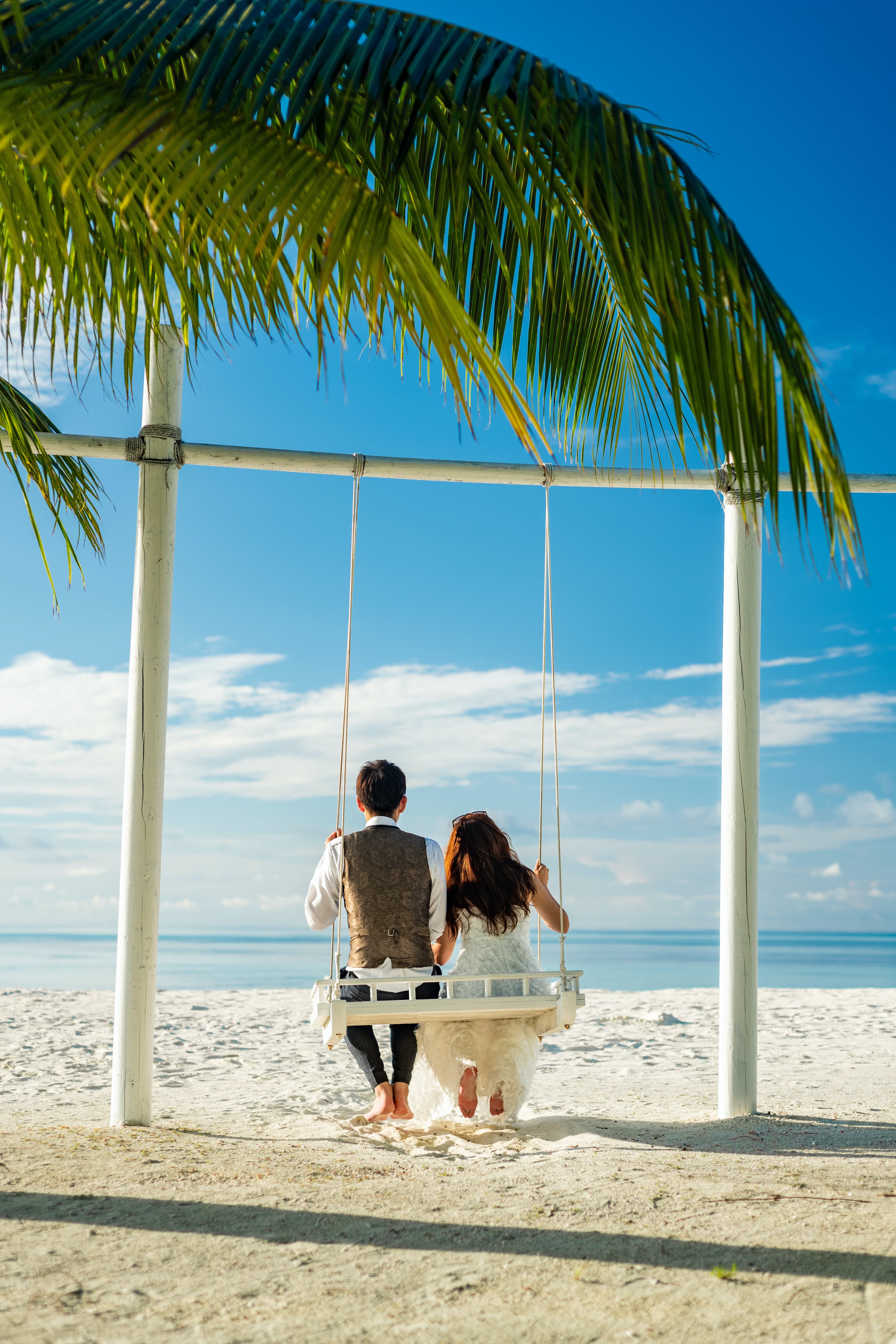 A couple sitting on a swing on a tropical beach.