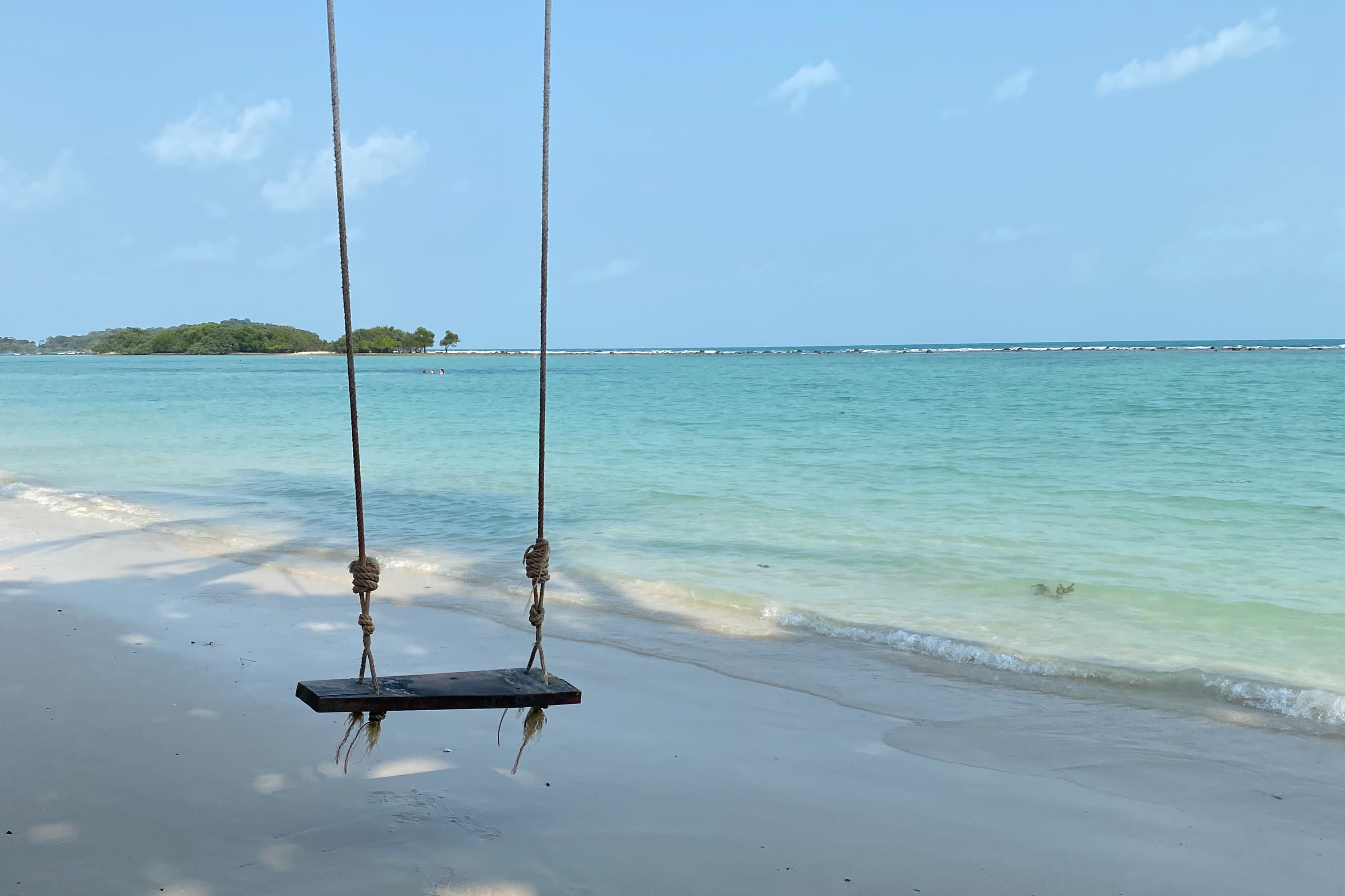 A swing on an island with blue water.
