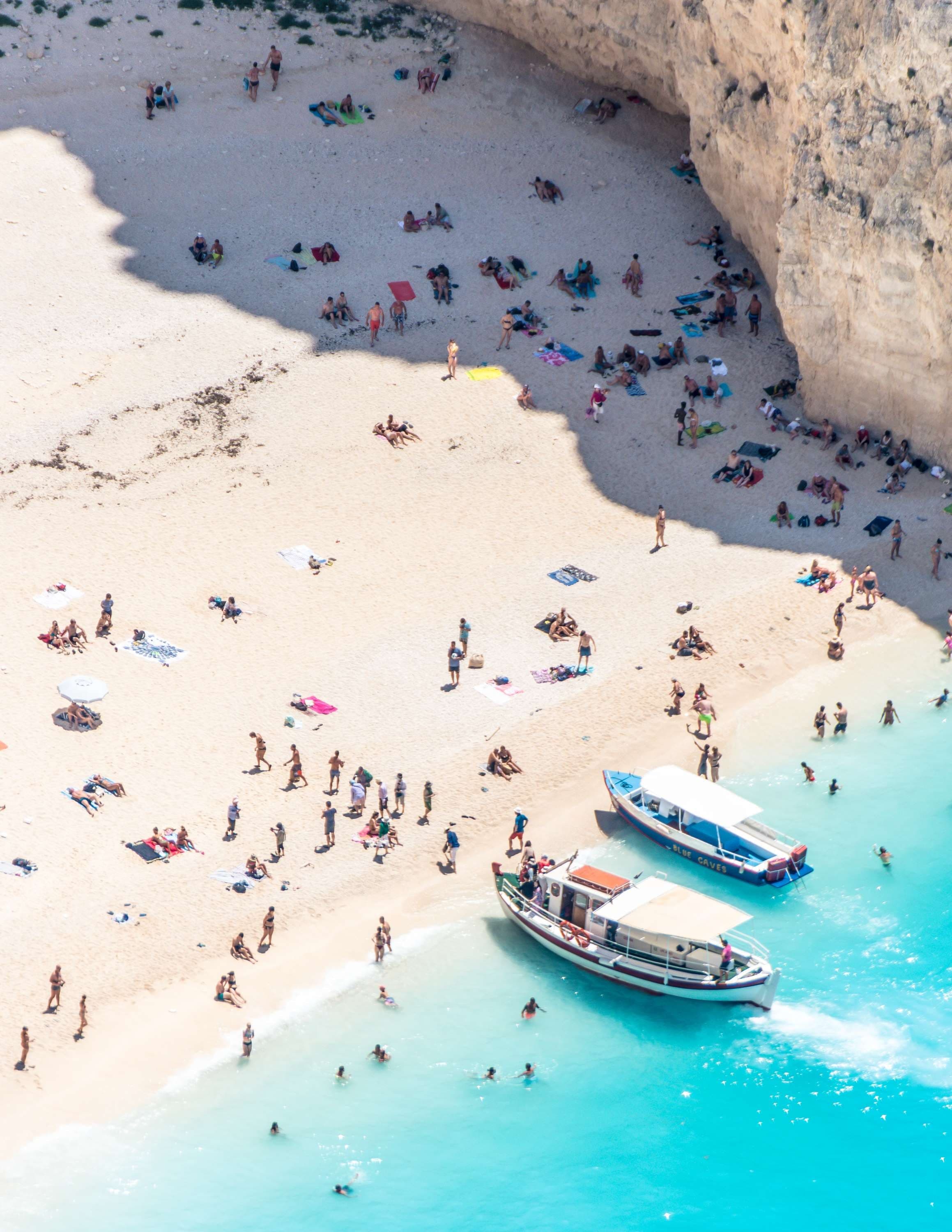 aerial view of people on a beach next to ocean and boats