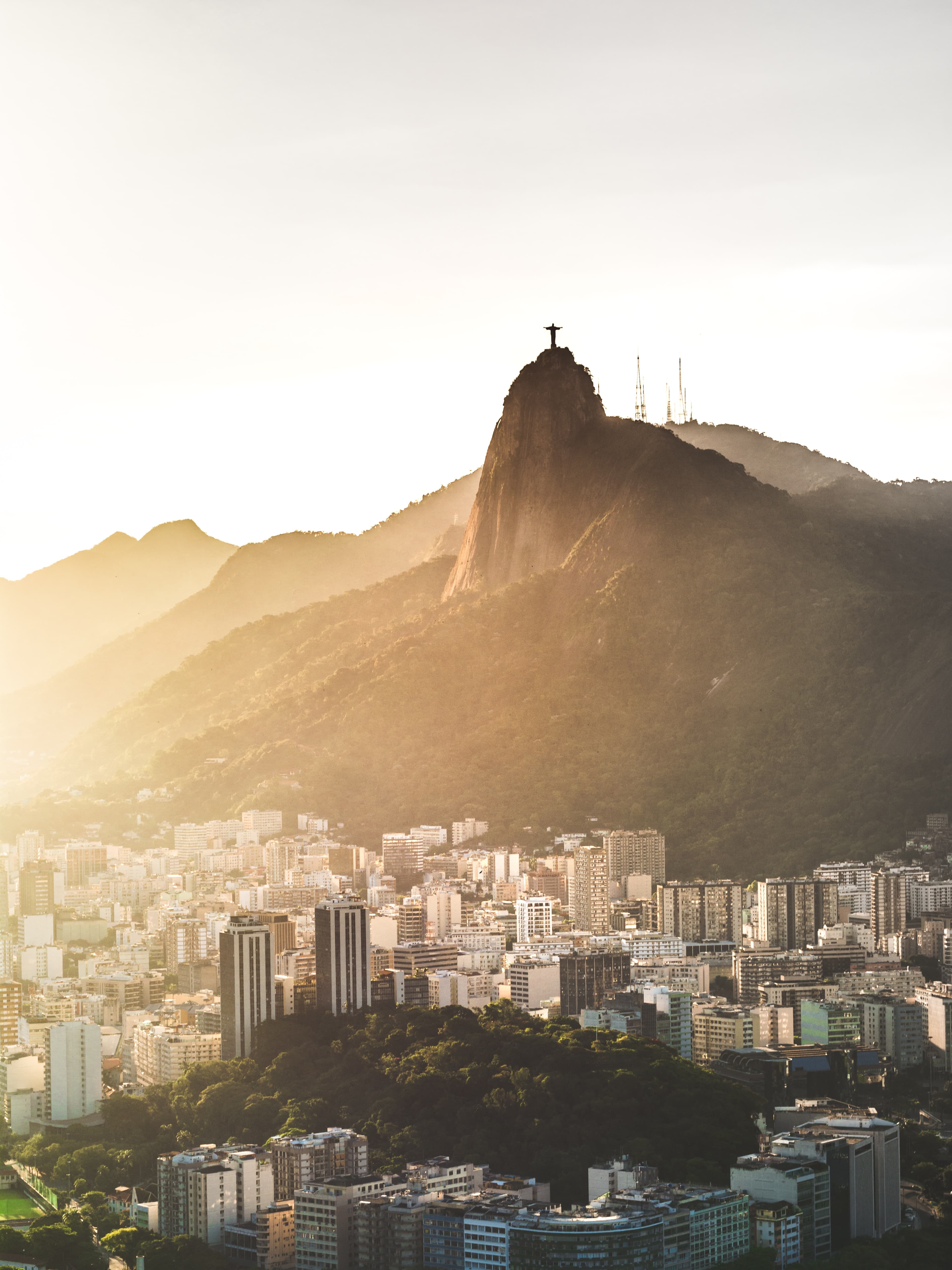 Sunset from Sugarloaf mountain in Rio de Janeiro in Brazil overlooking the city full of white buildings and the large drastic mountains.