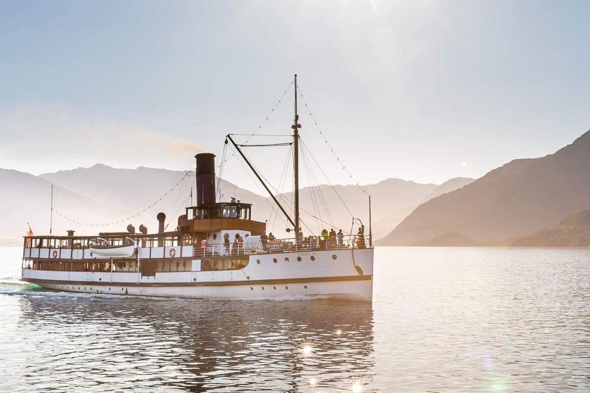 A cruise ship on sparkling water with mountains in the background.